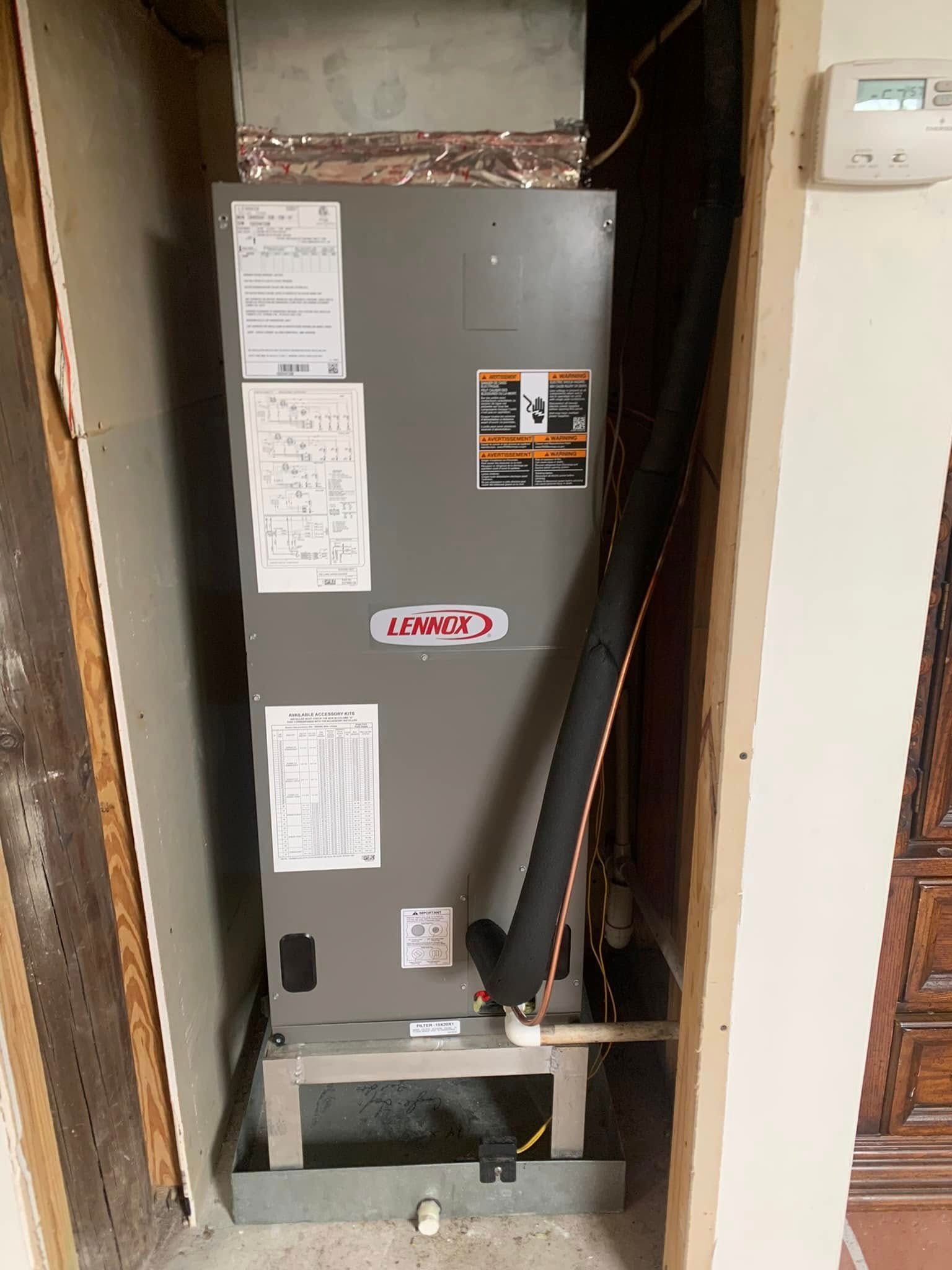 A gray HVAC air handler unit standing in a closet space on a metal stand with a drain pan beneath it.