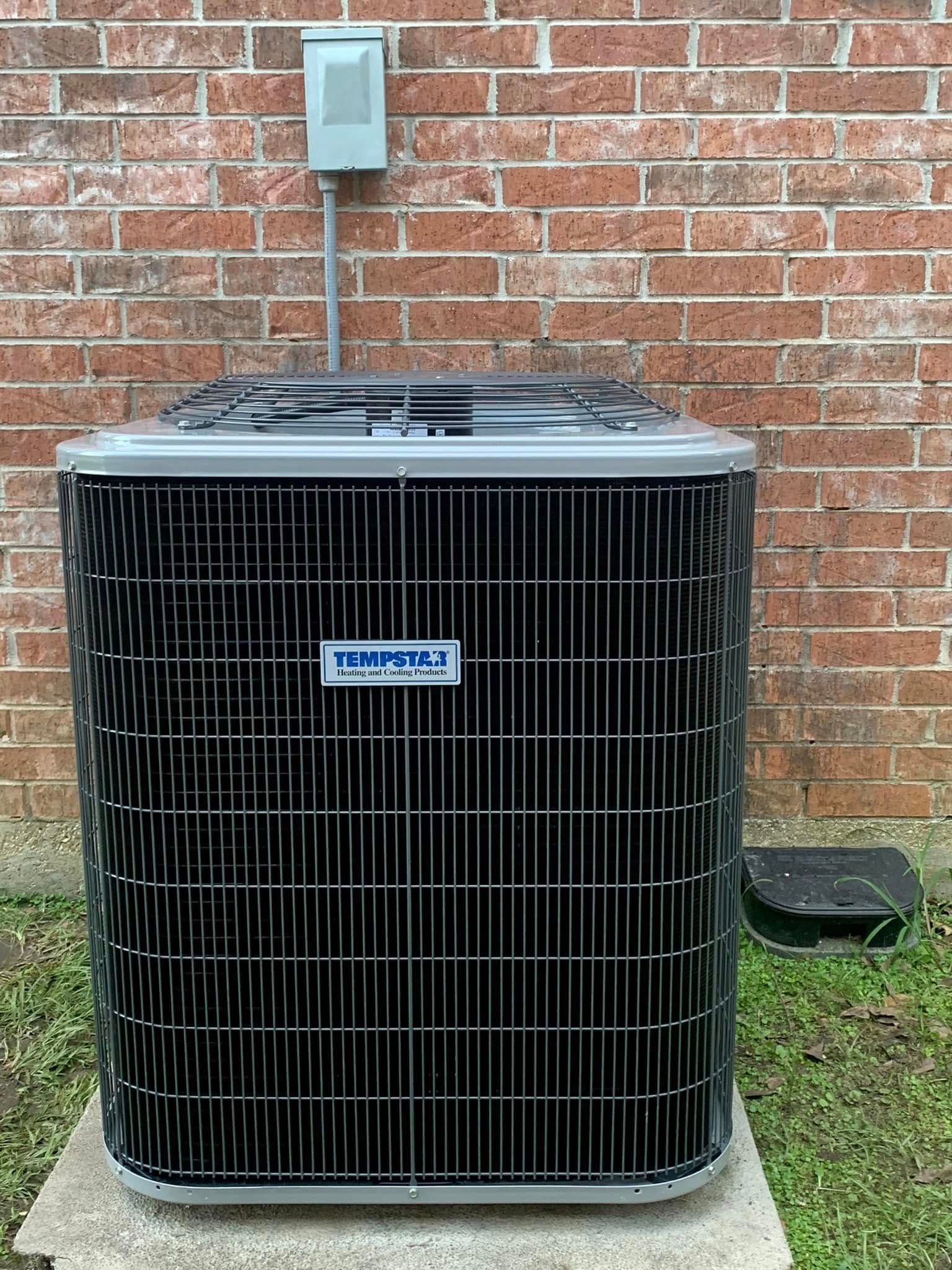 A Tempmaster outdoor HVAC unit sitting on a concrete pad against a red brick wall with a grey electrical disconnect box.