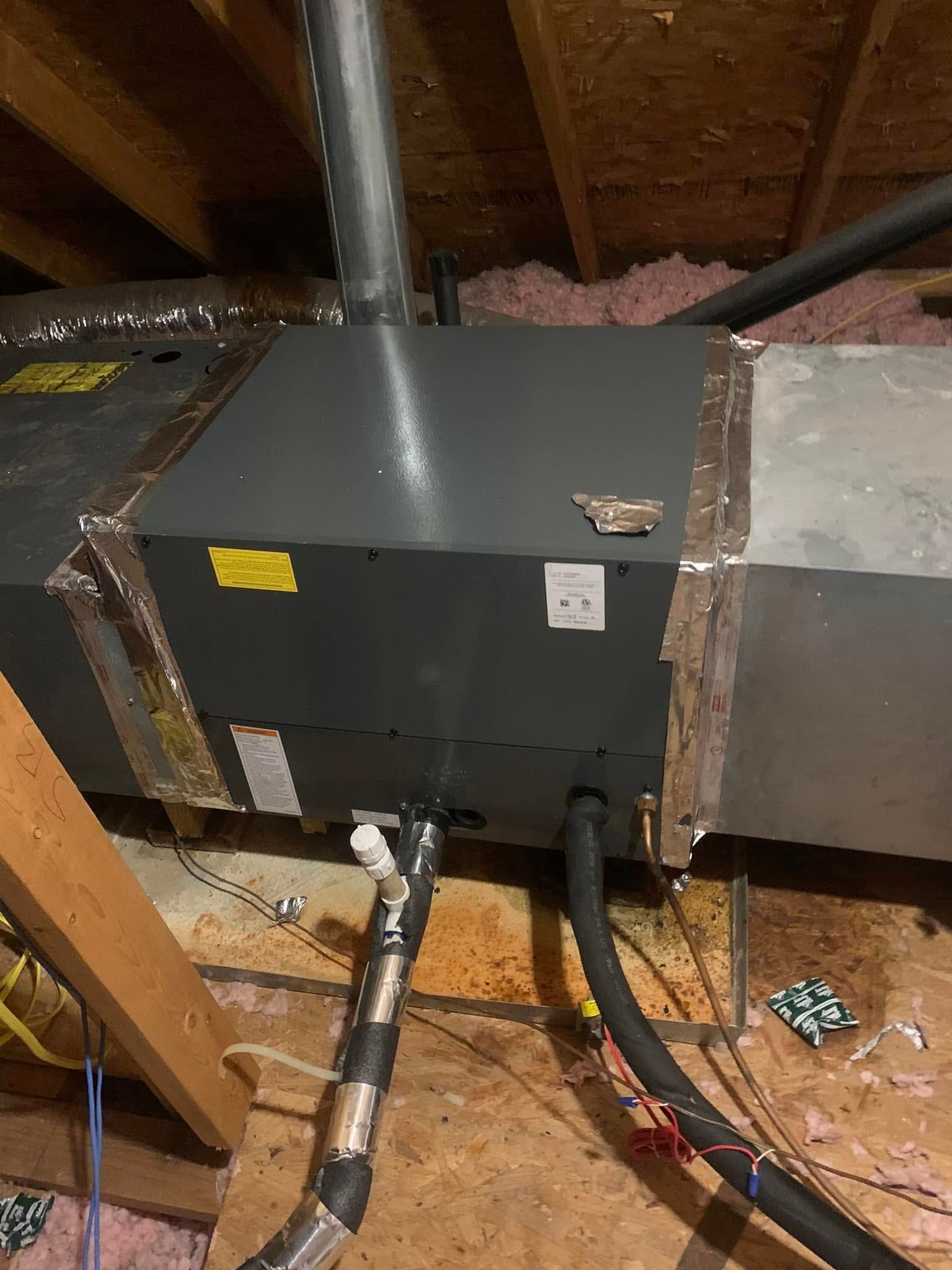 An HVAC air handler unit installed in an attic with insulated drain lines and ductwork connections visible.