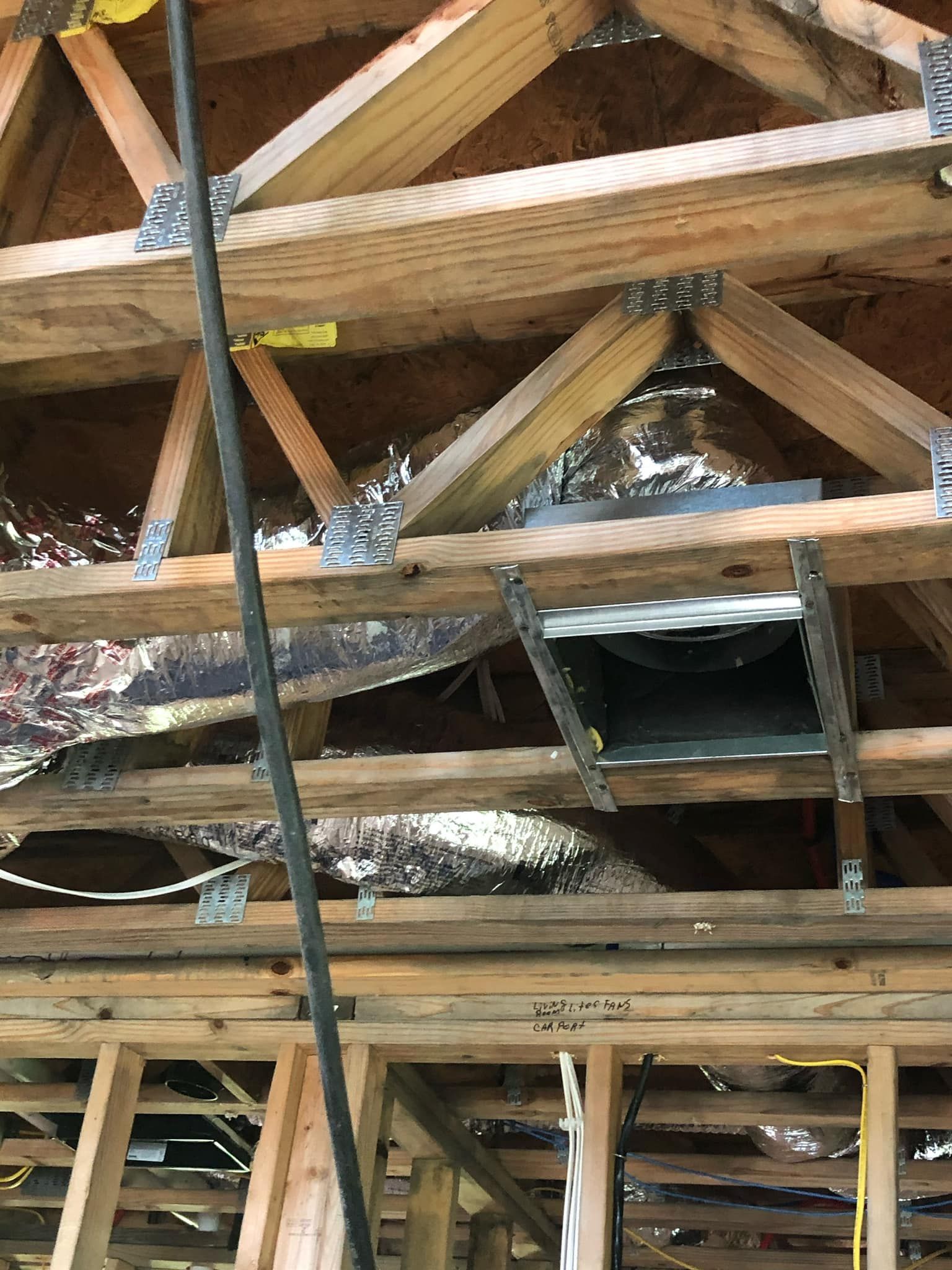 Framed wooden roof trusses and metal ductwork installed in an unfinished attic space.
