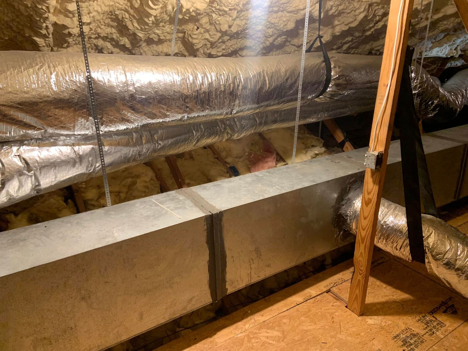 View of a residential attic showing metal rectangular and flexible insulated ductwork suspended from the rafters.