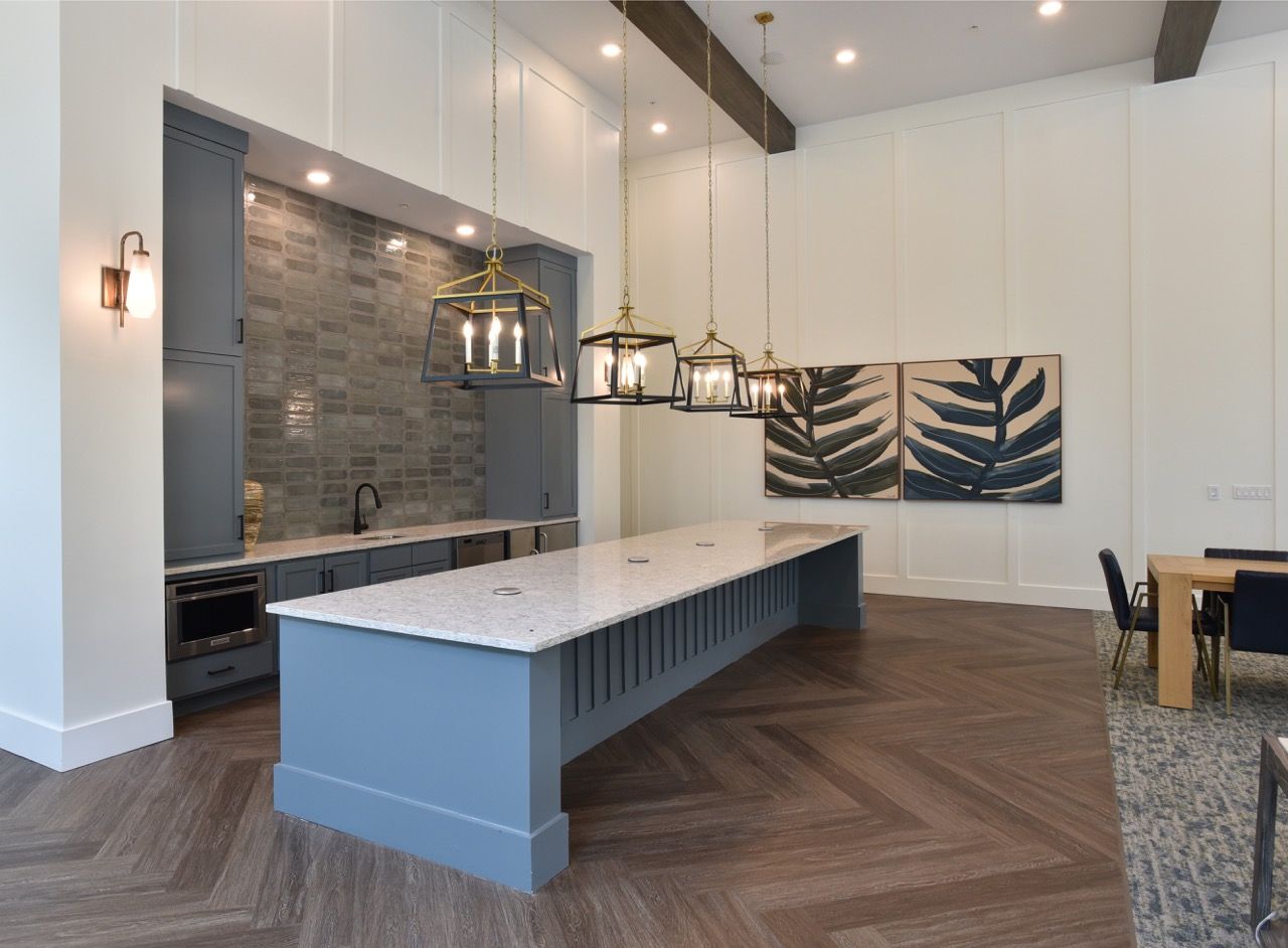 Modern apartment kitchen with a large central island, grey cabinetry, and pendant lights.