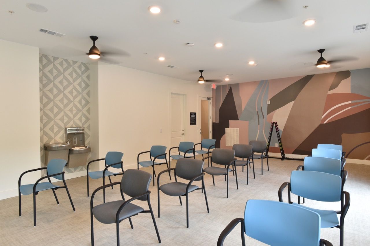 Interior community room with rows of blue and gray chairs and a geometric mural on the wall.