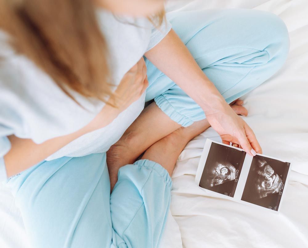 A pregnant woman is sitting on a bed holding a picture of her baby
