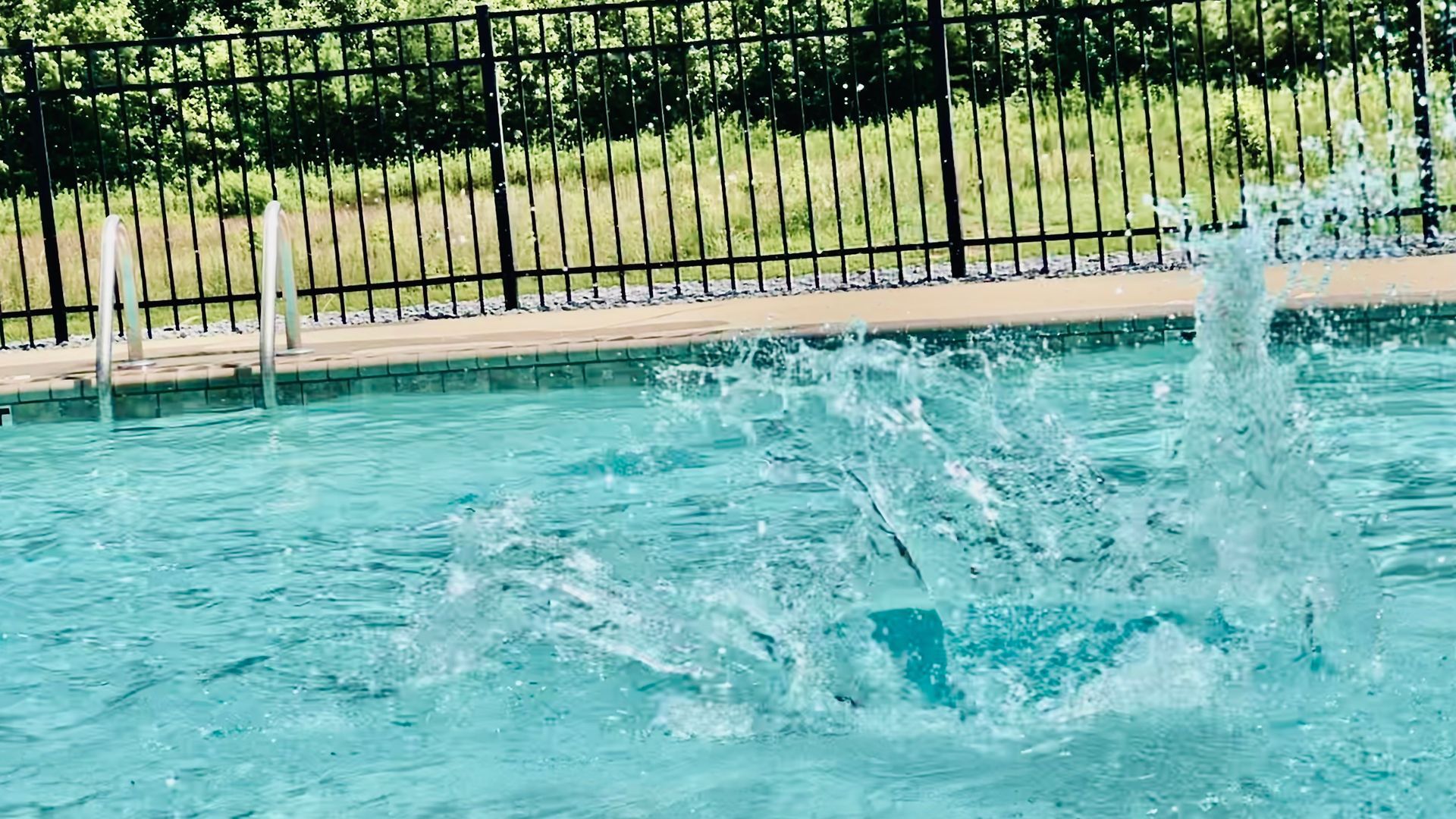 A person is jumping into a swimming pool with a fountain in the background.