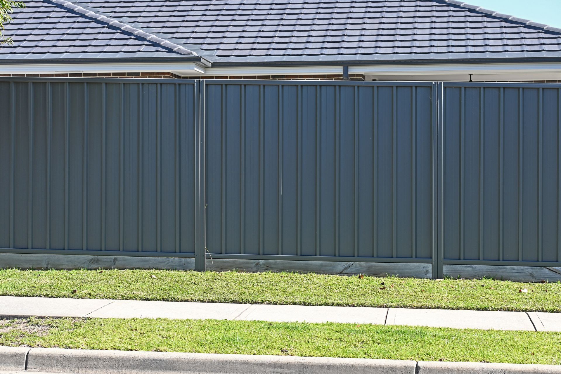 A gray fence is in front of a house with a slate roof.
