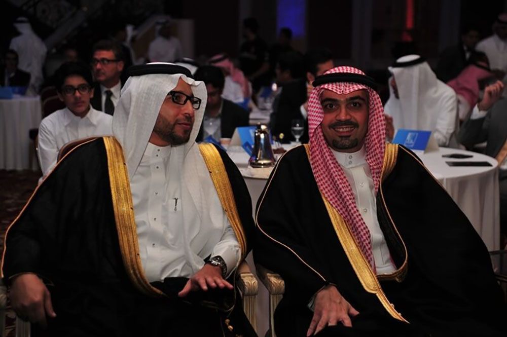 Two men in traditional Arab attire smiling in a formal setting.