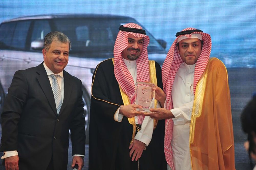 Three men at an event: two in traditional robes receiving an award from a man in a suit.