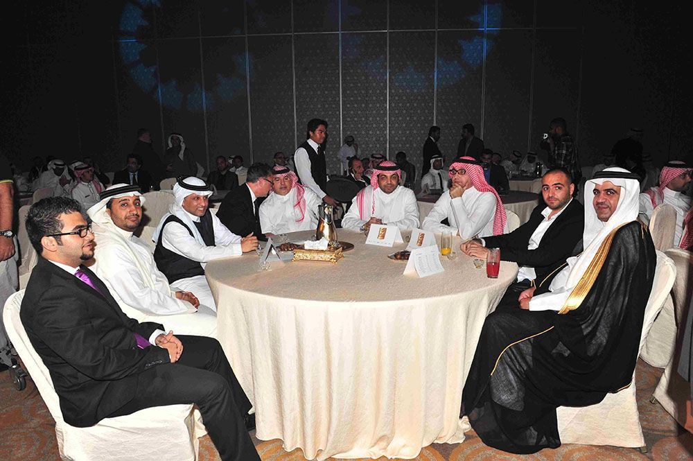 Men in traditional Arab attire and suits seated at round tables in a banquet hall.