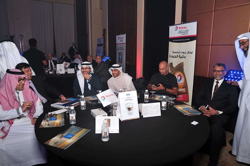 Group of men in formal attire at a table, some wearing traditional clothing, with promotional materials.