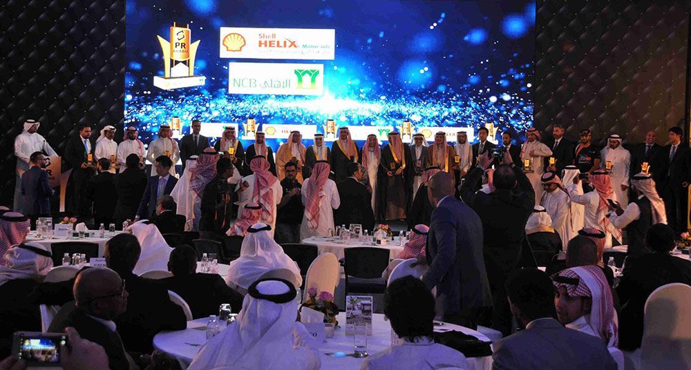 Awards ceremony with people in traditional dress on stage, crowd in formal attire.