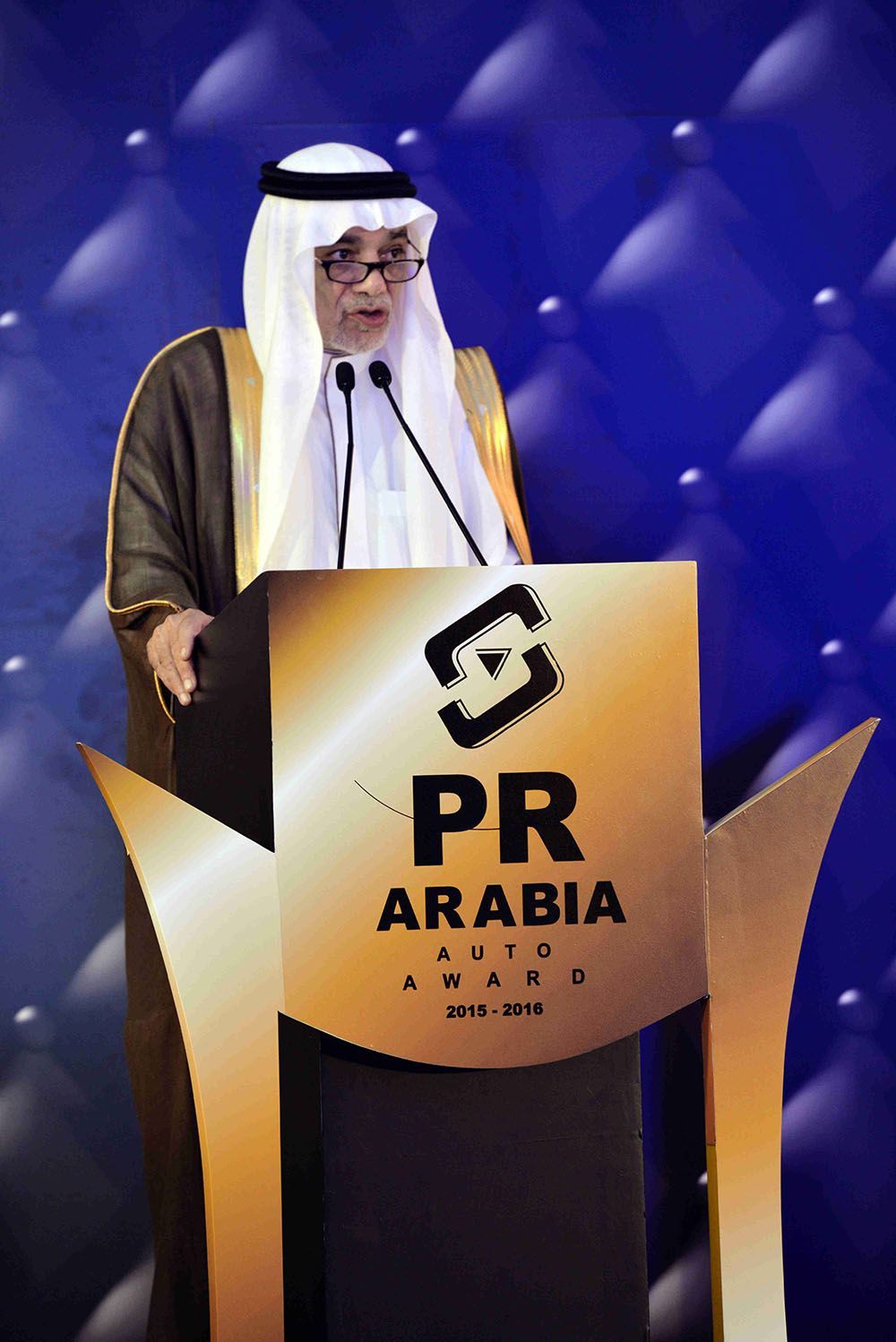 Man in traditional Arab dress speaking at PR Arabia event podium.