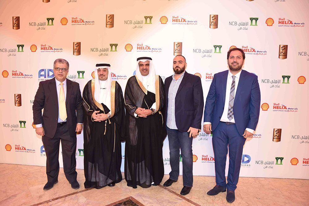 Five men in suits and traditional dress posing in front of a branded backdrop.