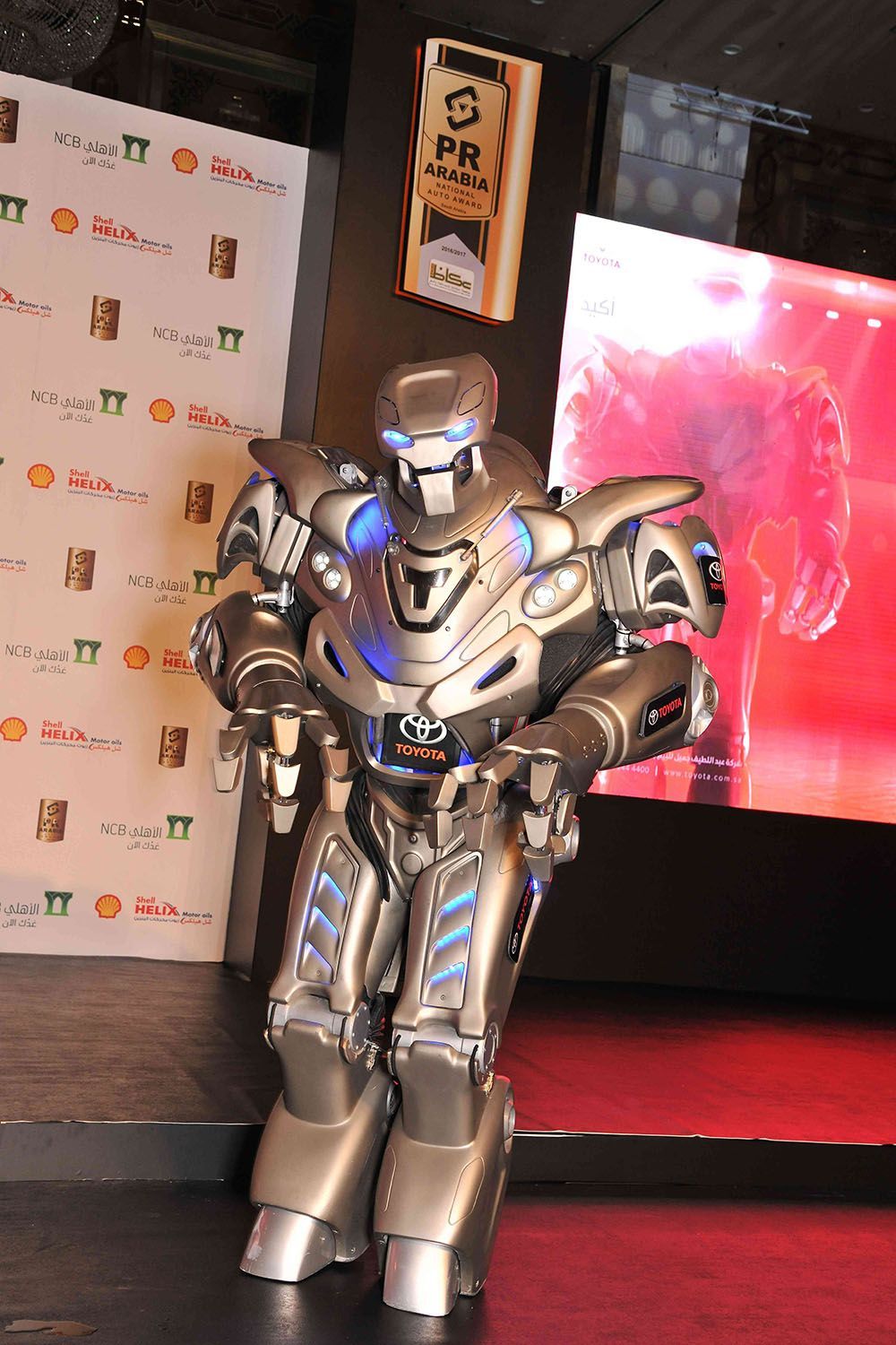 Robot entertainer with silver and blue accents, standing on a stage, arms forward.