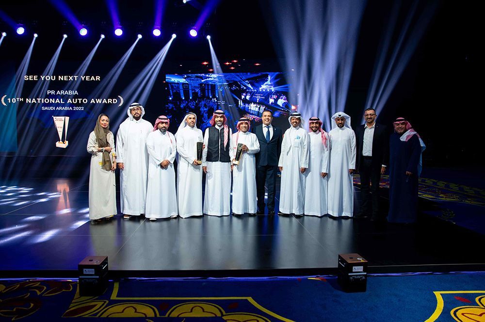 Group of people in traditional attire on stage at an event with a backdrop.