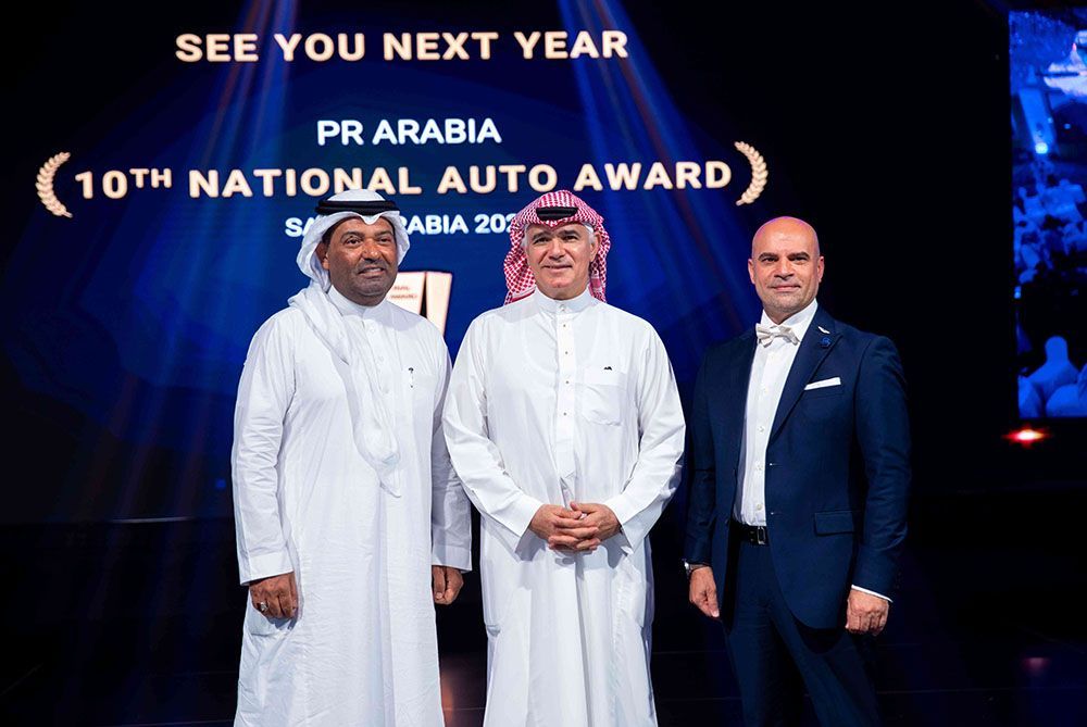Three men at the PR Arabia 10th National Auto Award in Saudi Arabia. Two in white robes, one in a suit.