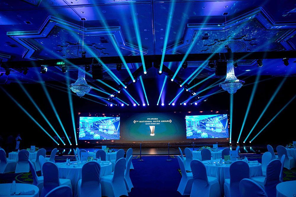 An awards ceremony stage illuminated with blue lights, tables set with white cloths.