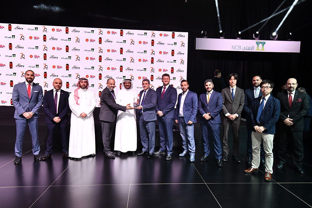 Group of men in suits and traditional attire receiving an award on a stage.