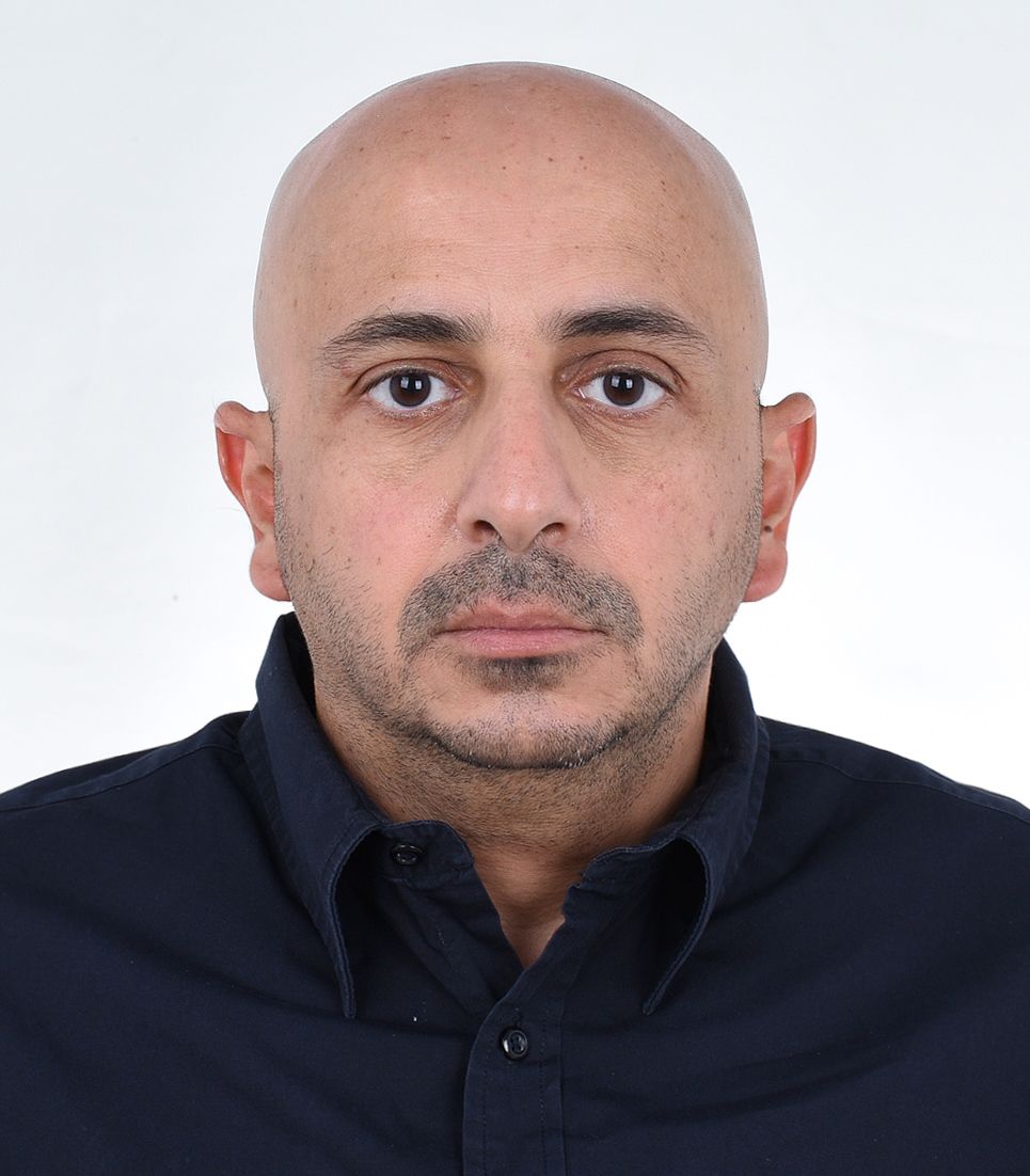 Bald man in a navy blue shirt, facing the camera with a neutral expression.