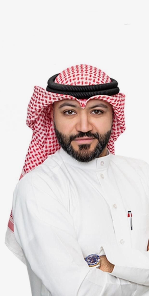 Man in traditional Arab attire, with red and white patterned headwear and white robe, looking at the camera.