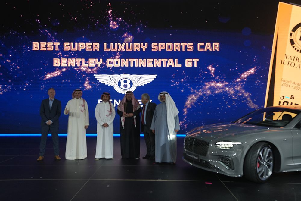Award ceremony with Bentley Continental GT. Group of men beside the car on a stage with blue backdrop.