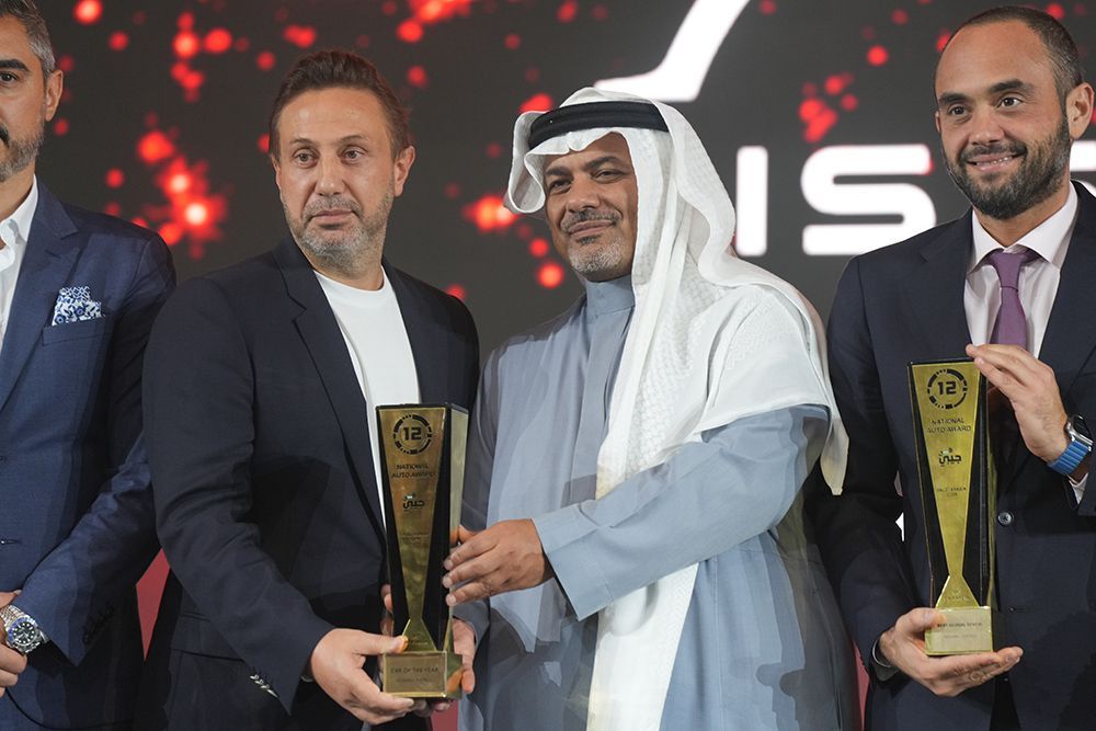 Men in suits holding awards at an event, one in traditional Arab dress.