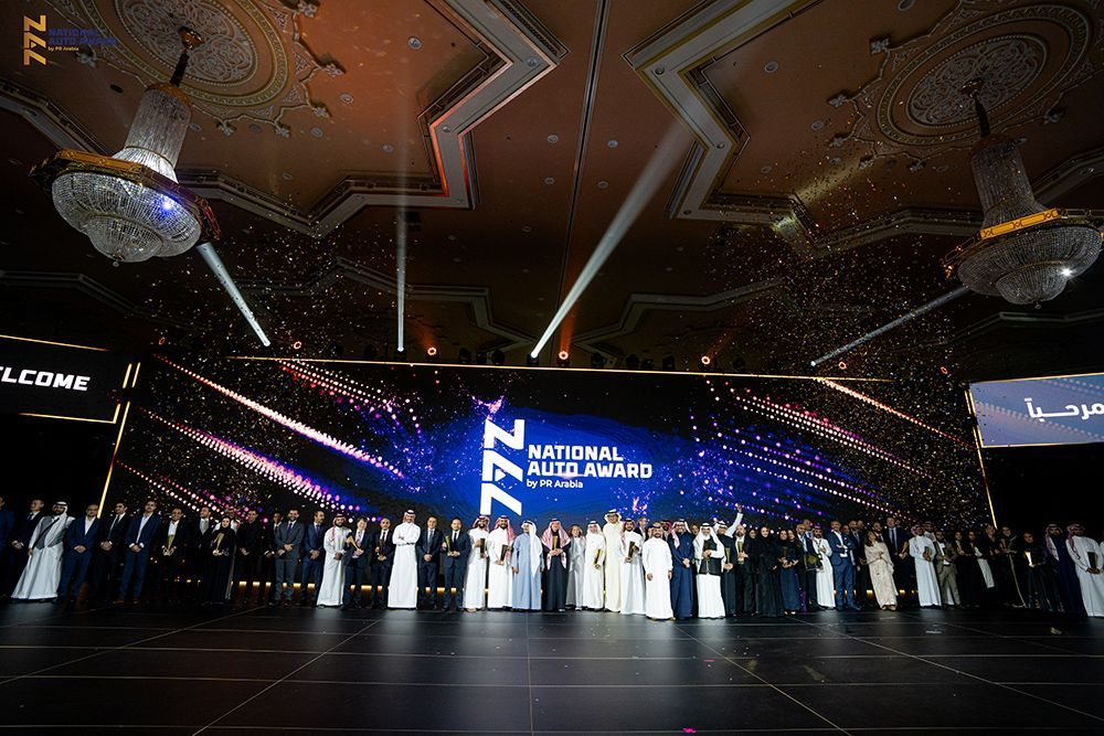 Group of people in formal wear on stage at an awards ceremony, with a large screen backdrop.