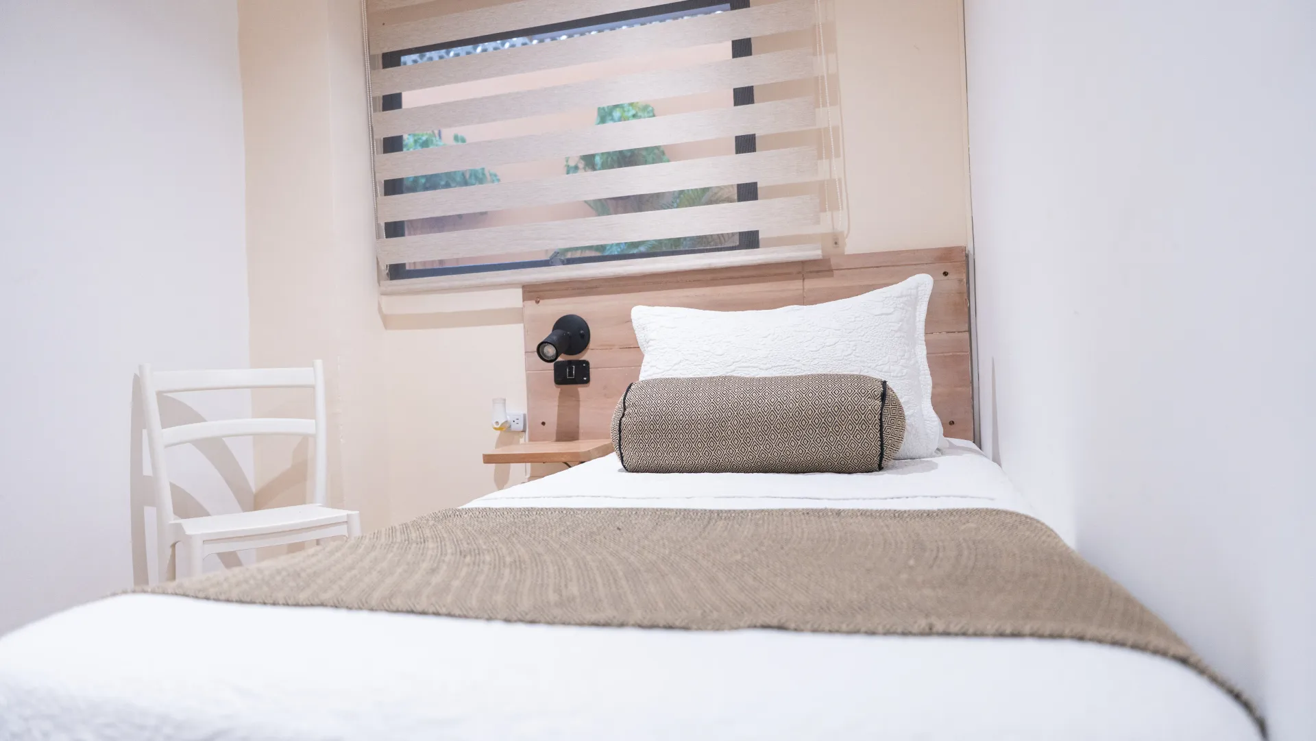 Un dormitorio con una cama individual, silla, mesa y ventana.