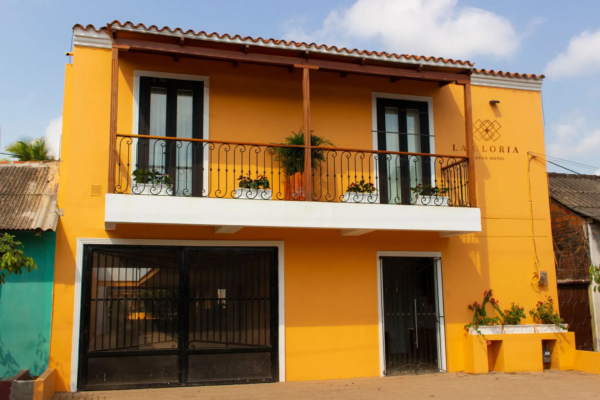 A yellow exterior of the La Gloria Hotel at Mompox with a balcony and a fence