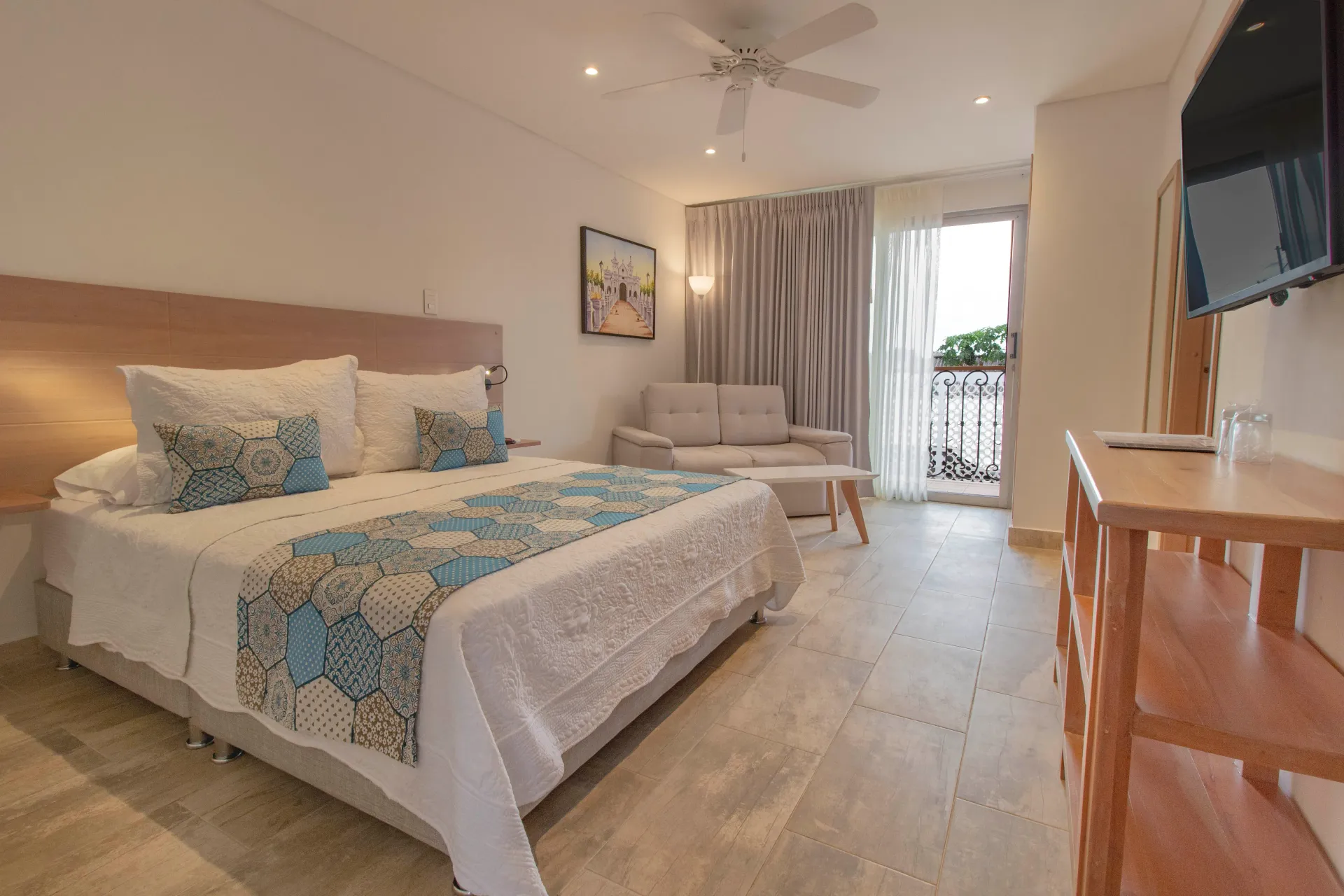 Una habitación del hotel La gloria en Mompox Colombia con una cama tamaño king, un sofá, un televisor y un balcón.