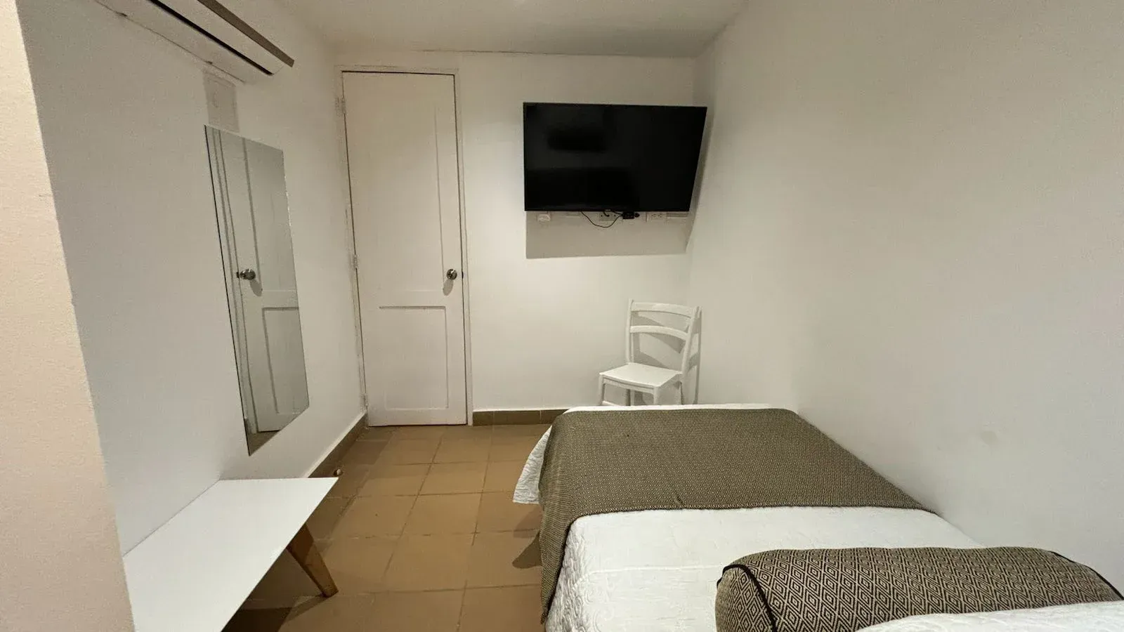 Un dormitorio con una cama, una silla, una televisión y un espejo.