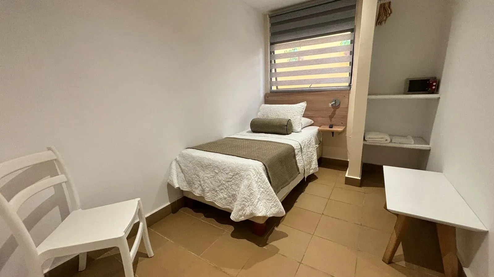 Un dormitorio con una cama individual, silla, mesa y ventana.