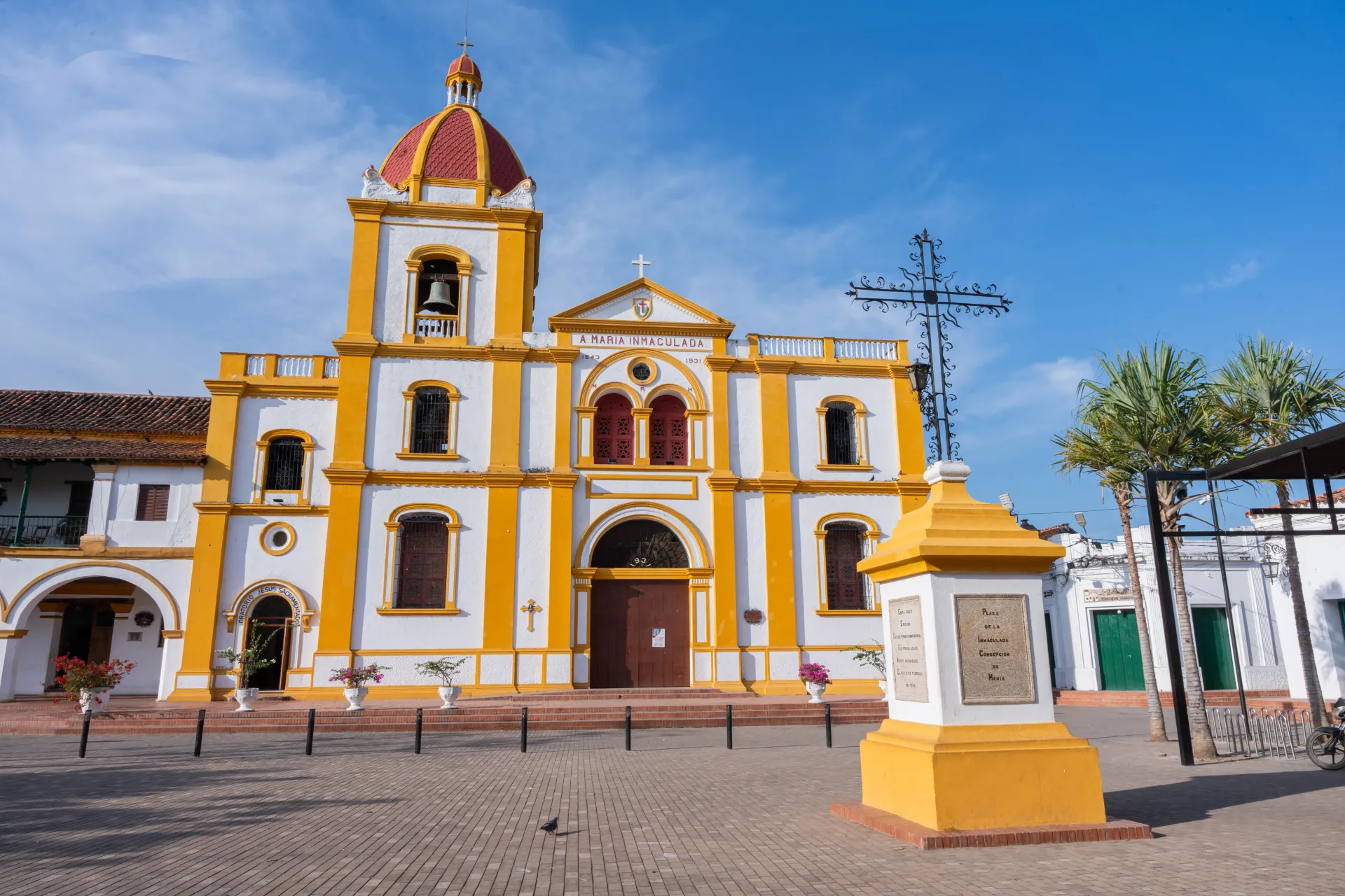 Una gran iglesia amarilla y blanca con una cruz delante de ella.