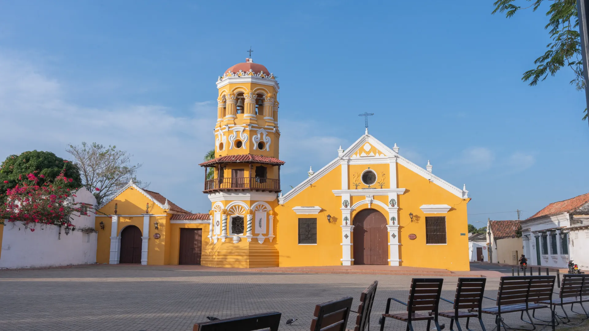 Una iglesia amarilla con una torre de reloj en el medio de una plaza.