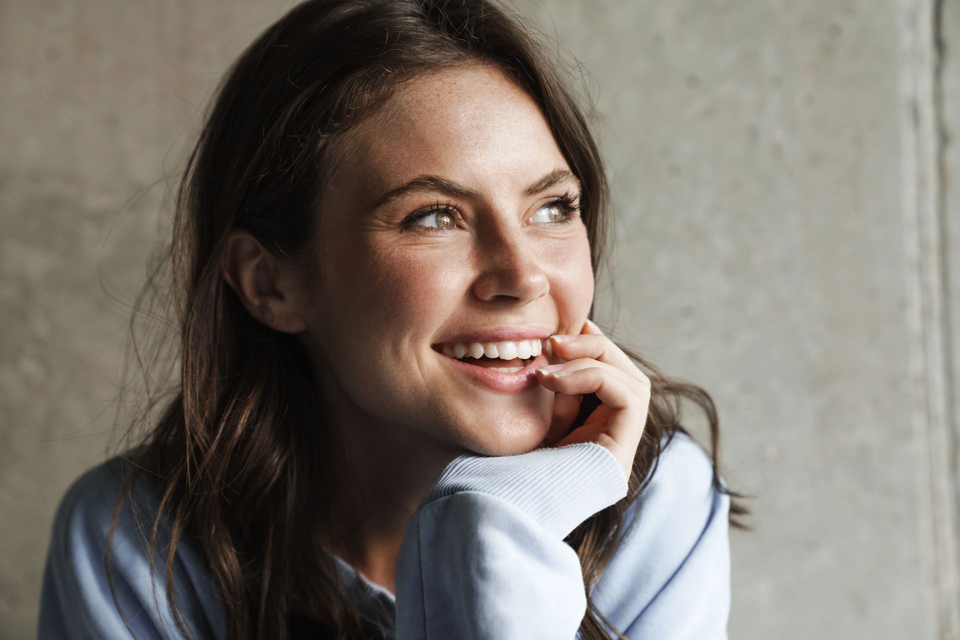 A close up of a woman smiling with her hand on her chin.