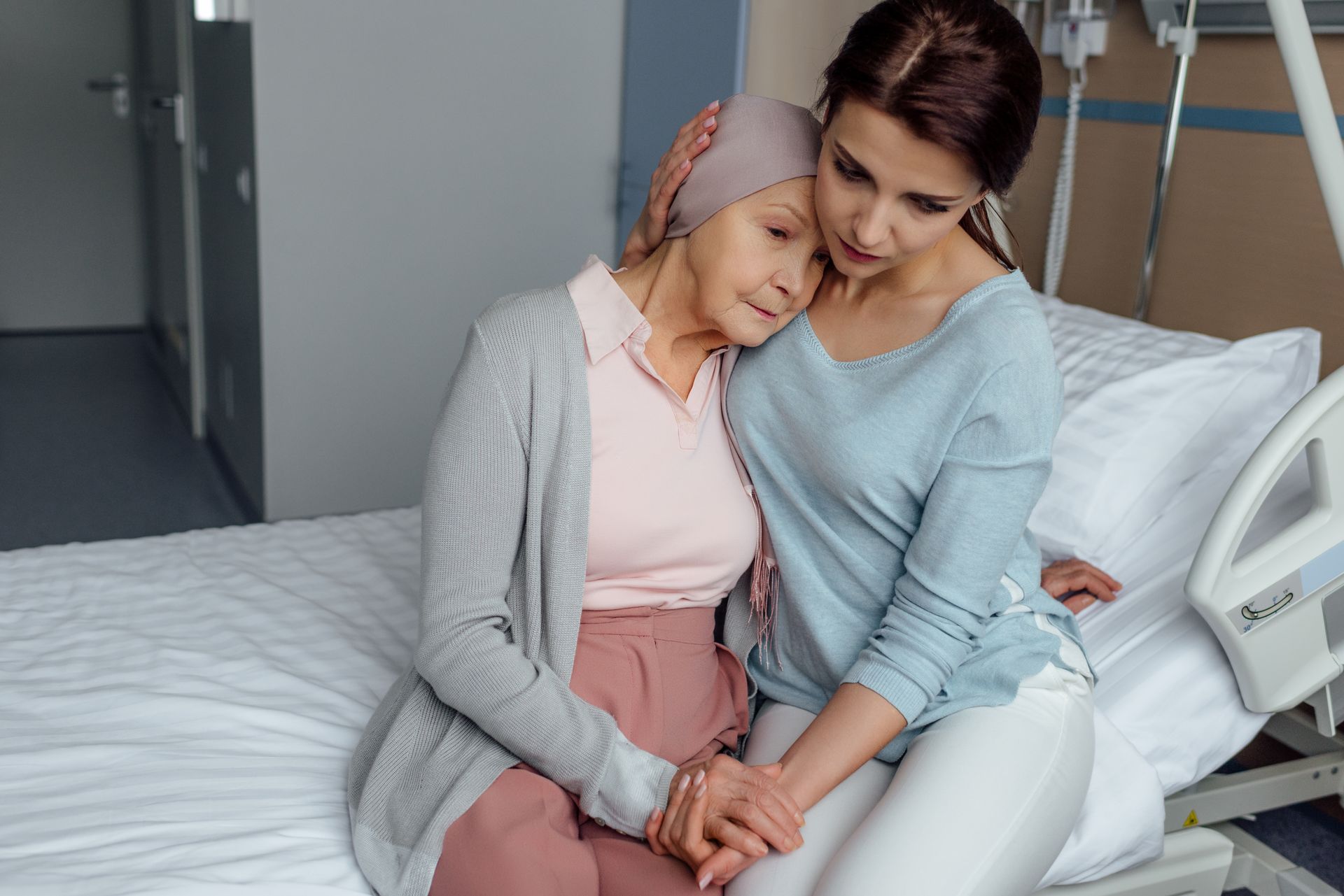 PTSS Voorbij-Holistisch herstel van PTSS en Trauma-Johan Reinhoudt-Jonge vrouw troost senior vrouw met kanker-zittend op rand ziekenhuisbed