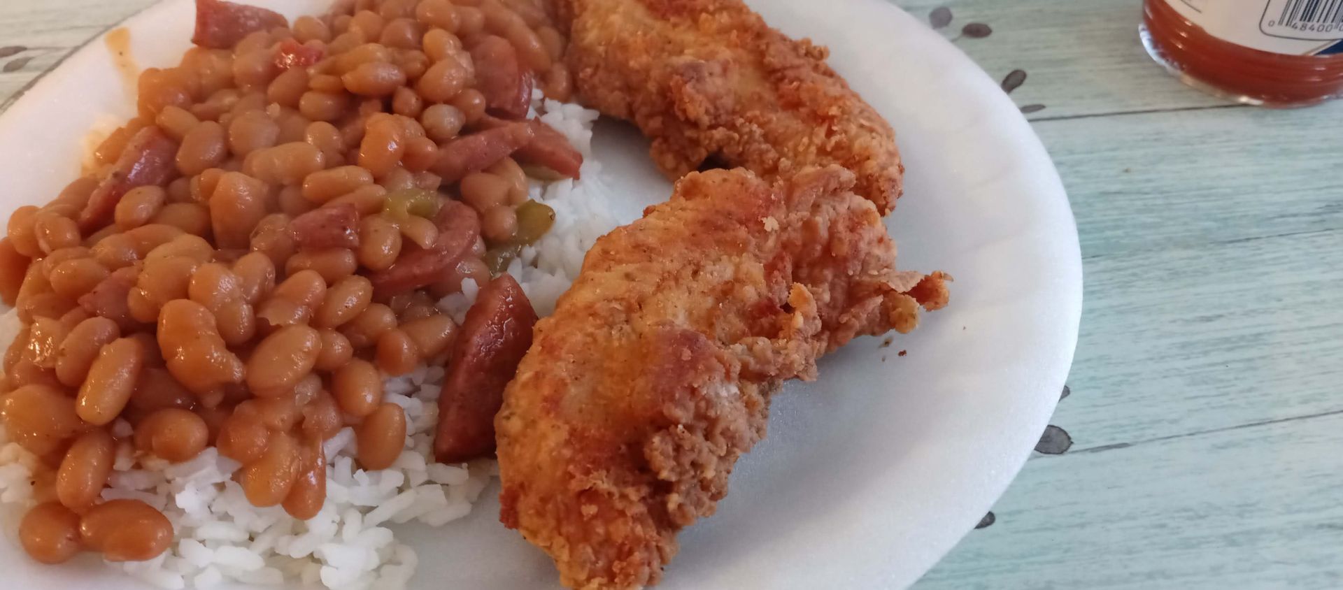 A white plate topped with fried chicken , rice and beans.