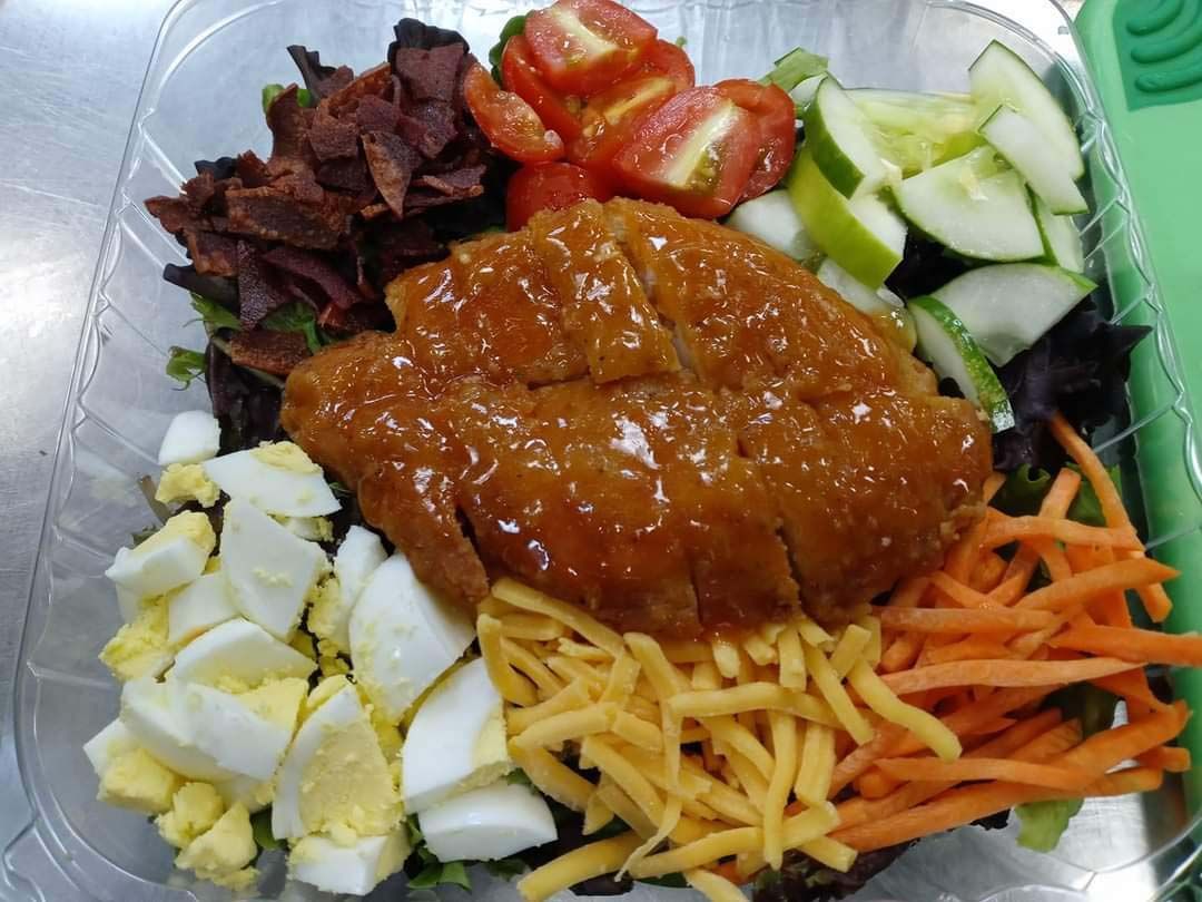 A salad with chicken , eggs , cheese , carrots and tomatoes in a plastic container