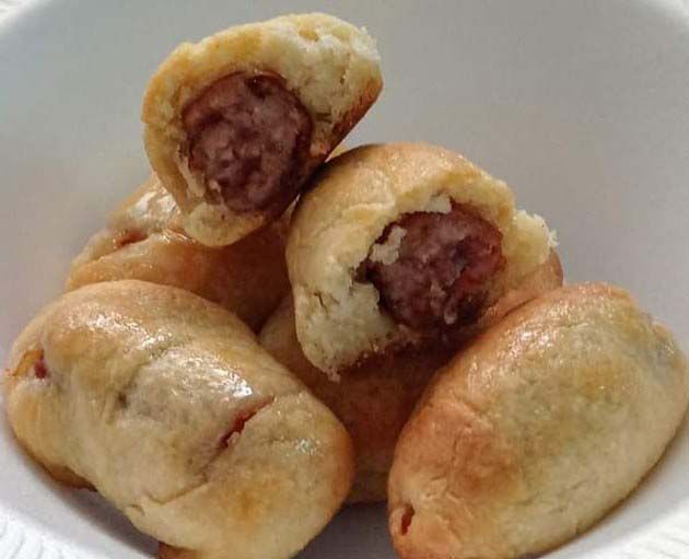 A bowl of sausage rolls with a bite taken out of one