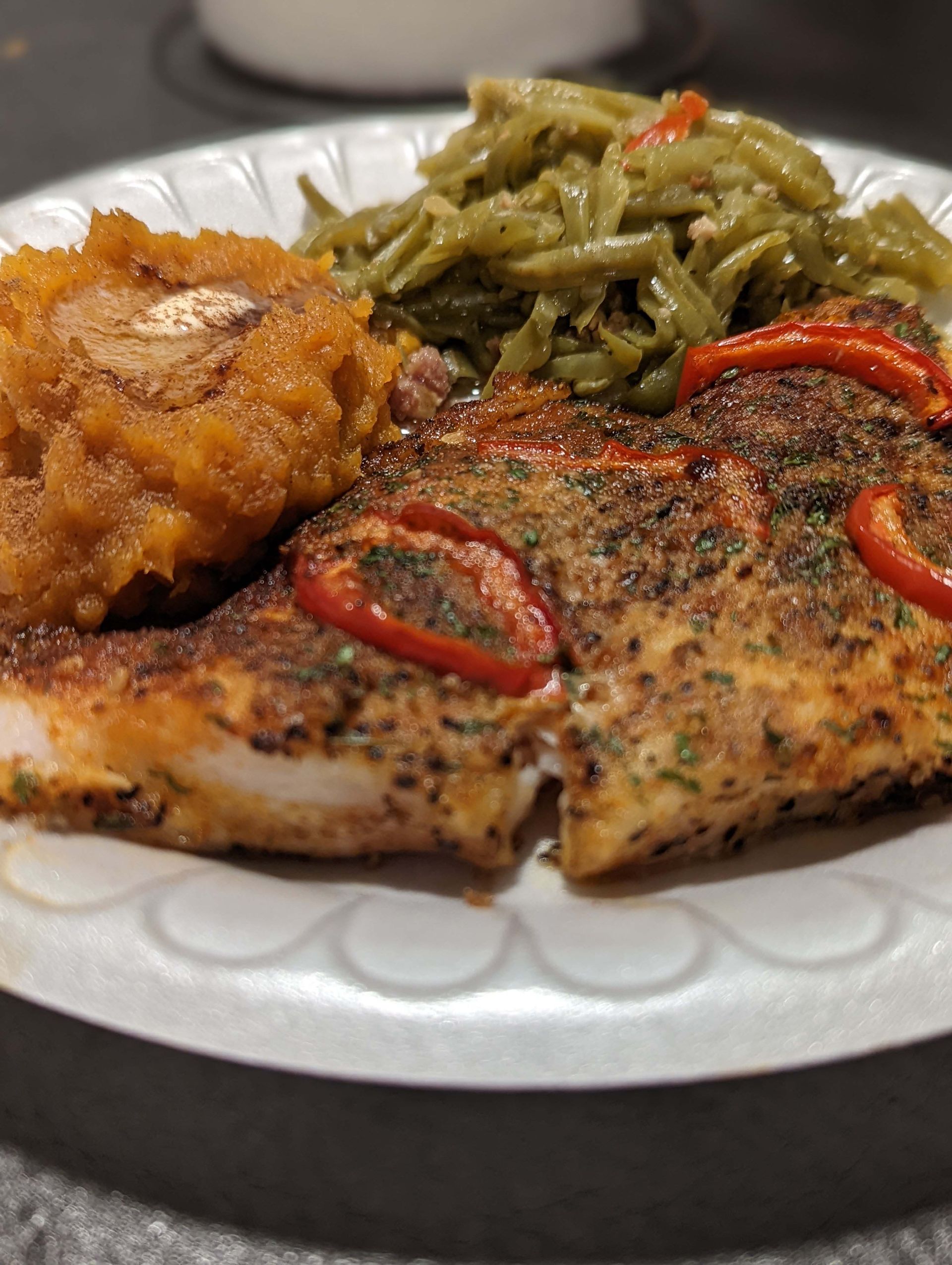 A paper plate topped with chicken , green beans and mashed potatoes.