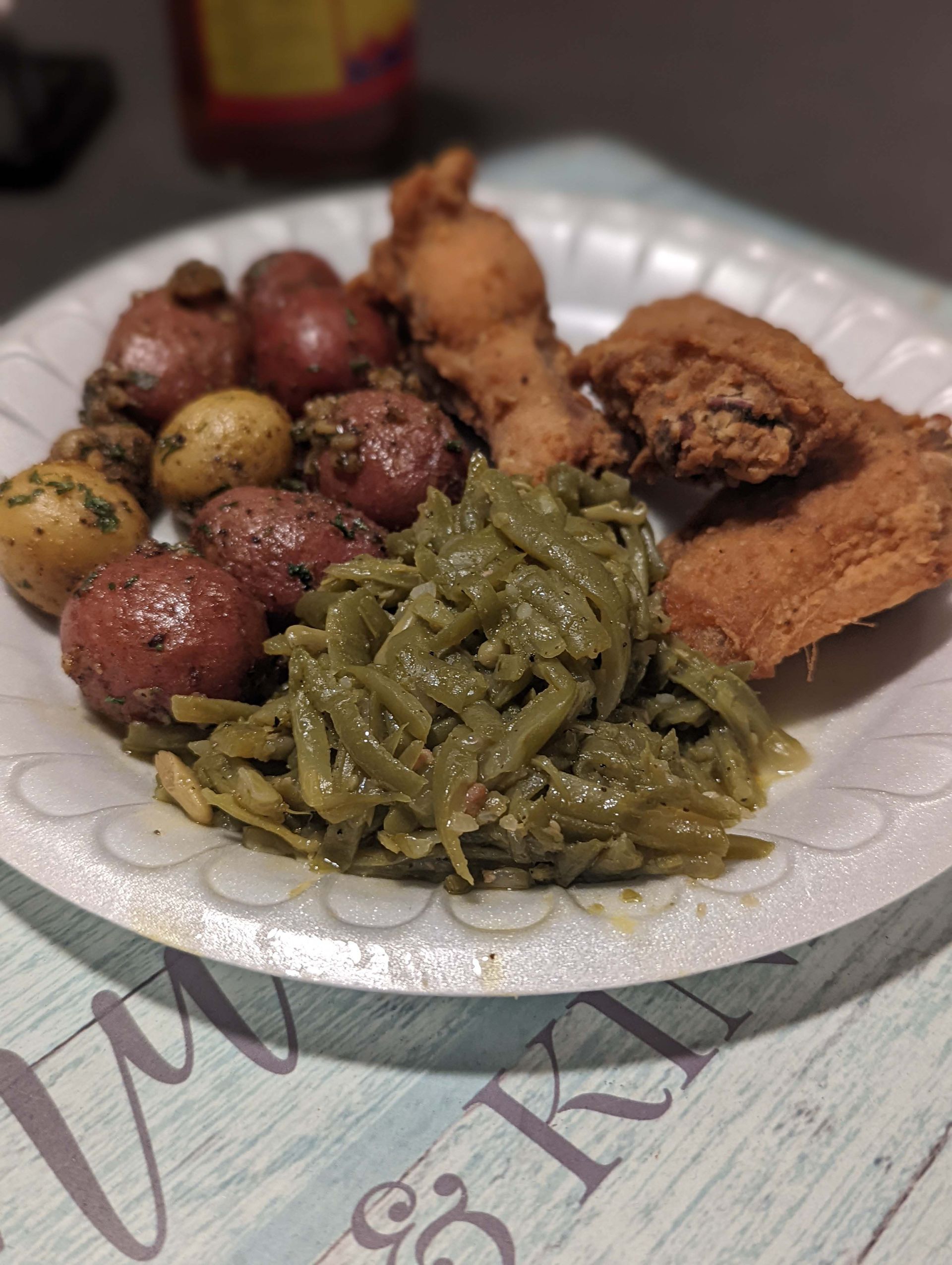 A paper plate topped with fried chicken green beans and potatoes