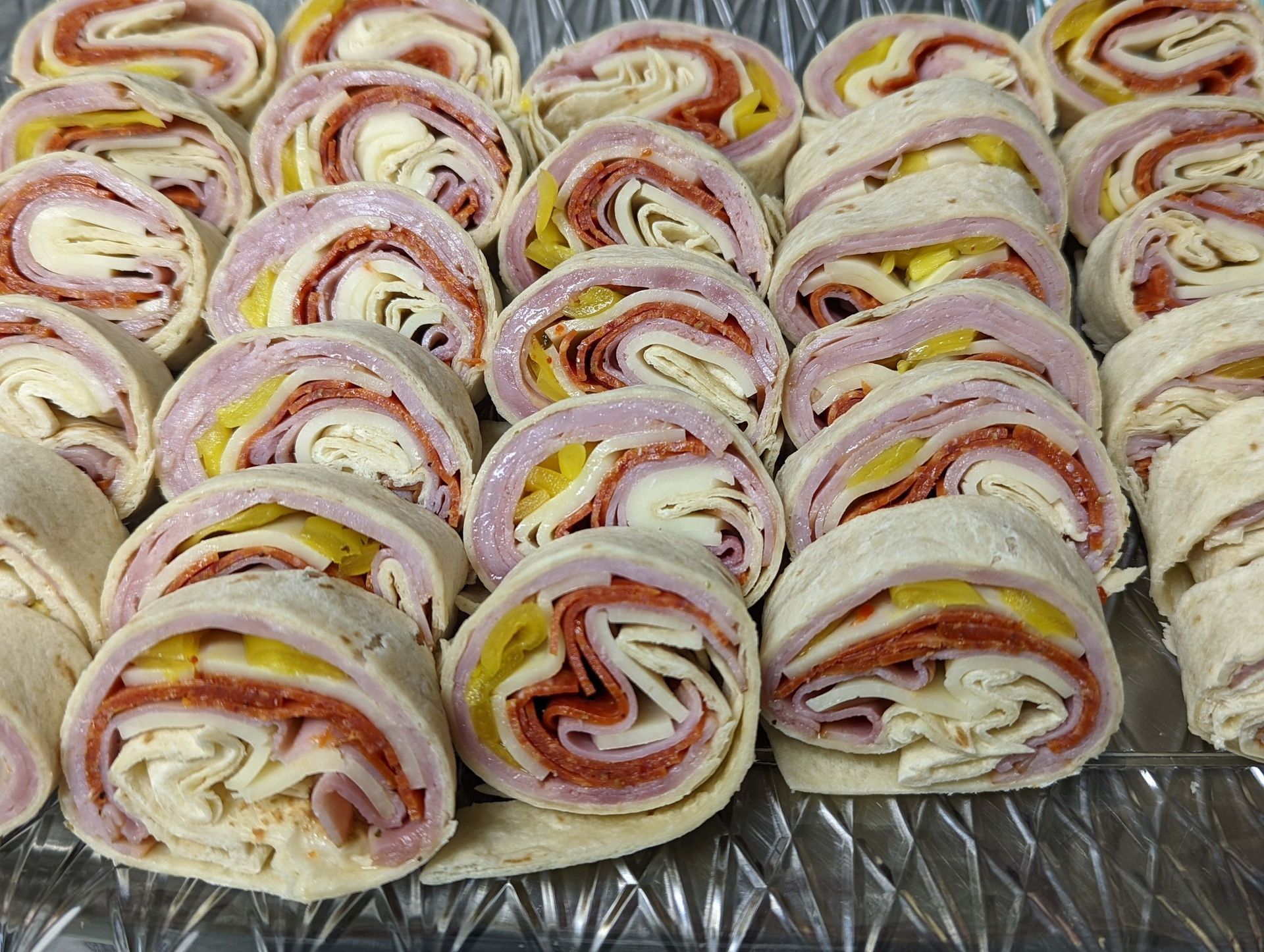 A tray of wraps with ham , cheese and pepperoni on a metal surface.