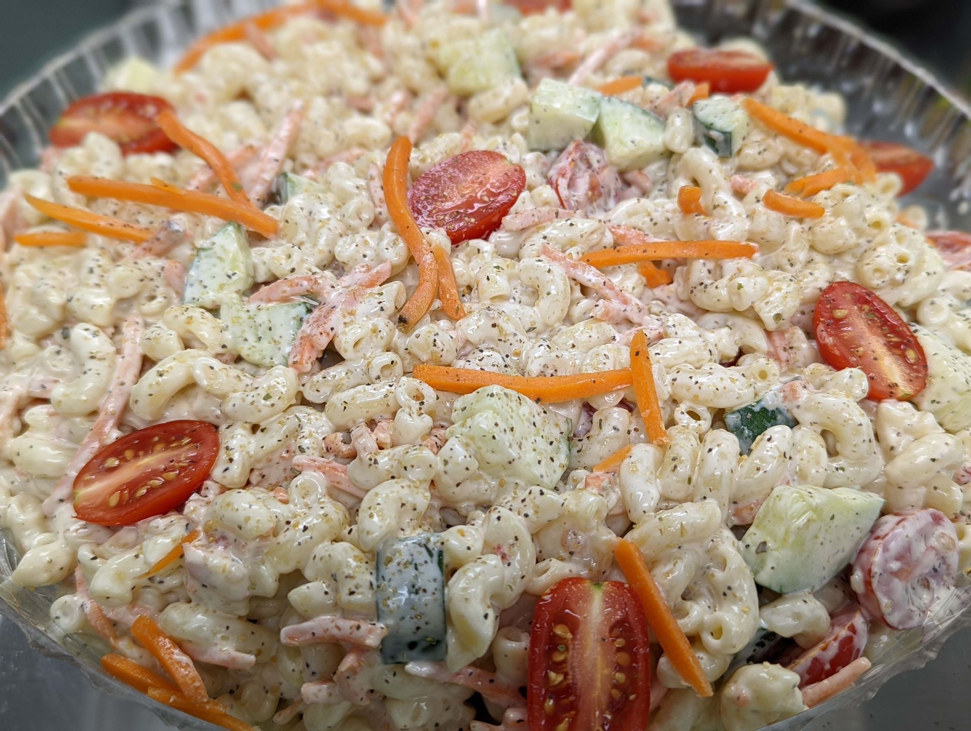 A macaroni salad with tomatoes , carrots , cucumbers and mayonnaise in a glass bowl.