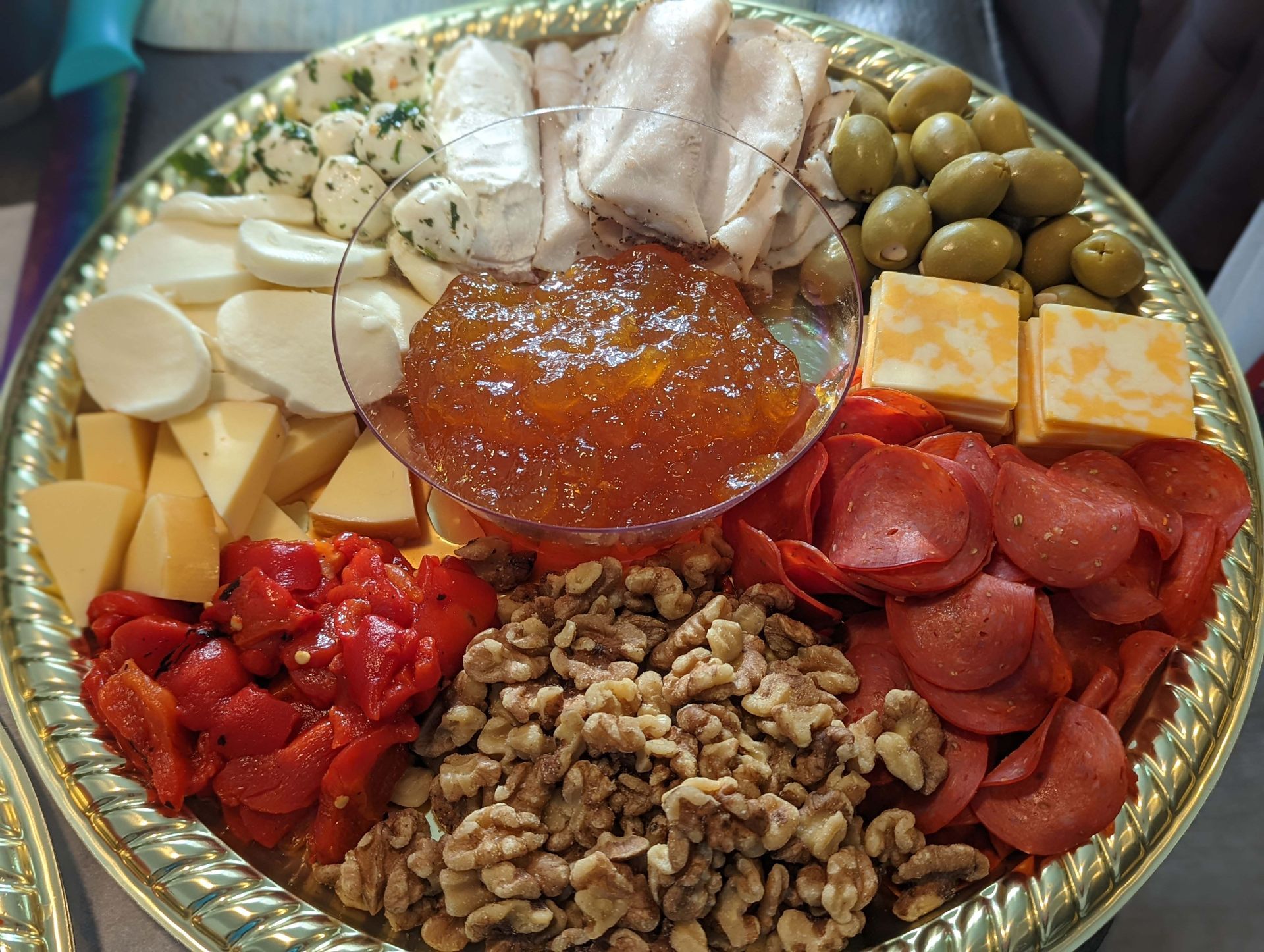 A tray of food including cheese , pepperoni , olives , walnuts and sauce.