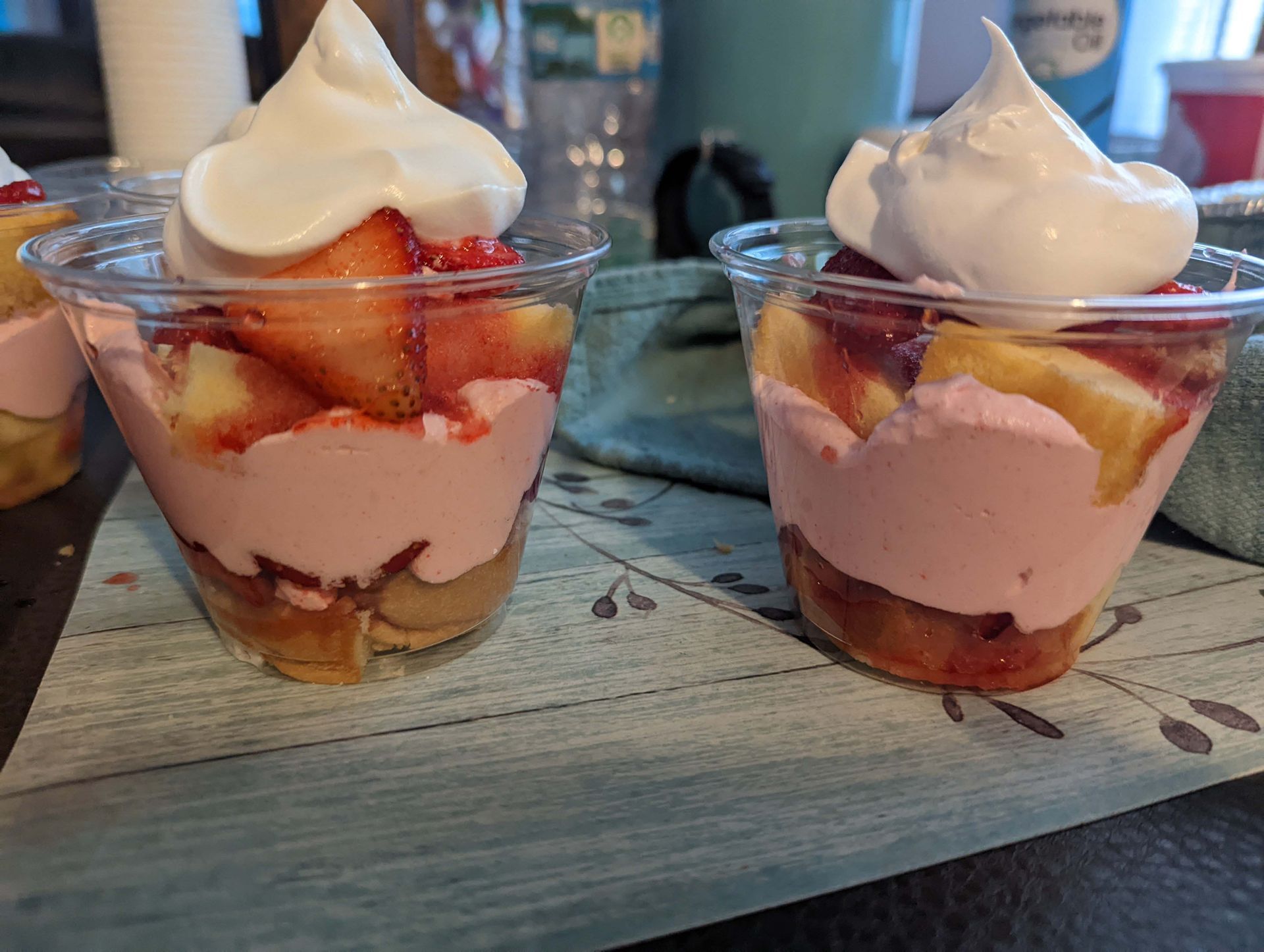 Two cups of dessert with whipped cream and strawberries on a table.
