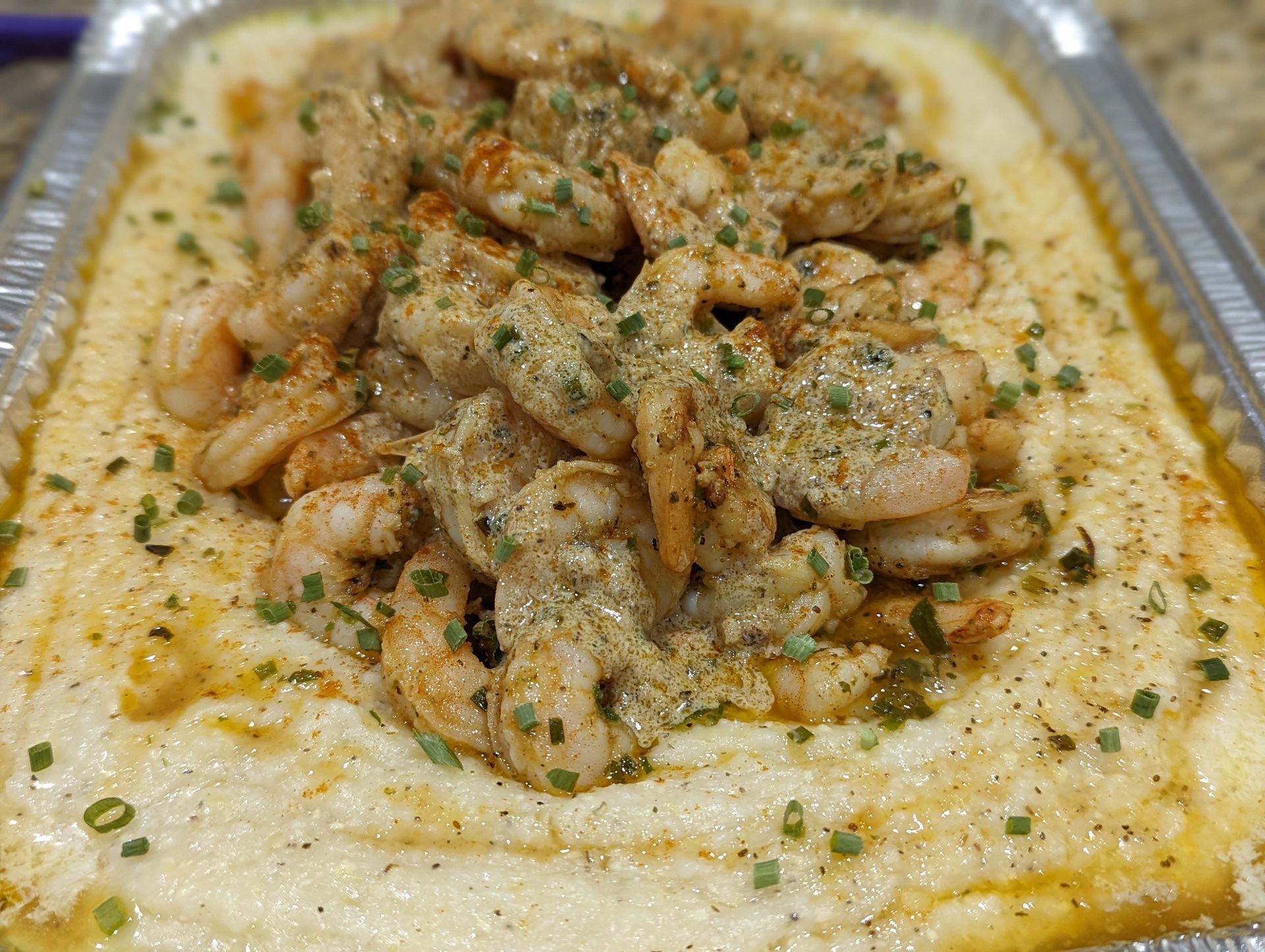 A close up of a tray of shrimp and grits on a table.