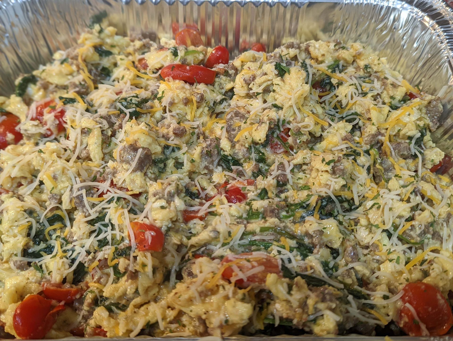 A casserole dish filled with scrambled eggs , cheese , tomatoes and spinach.