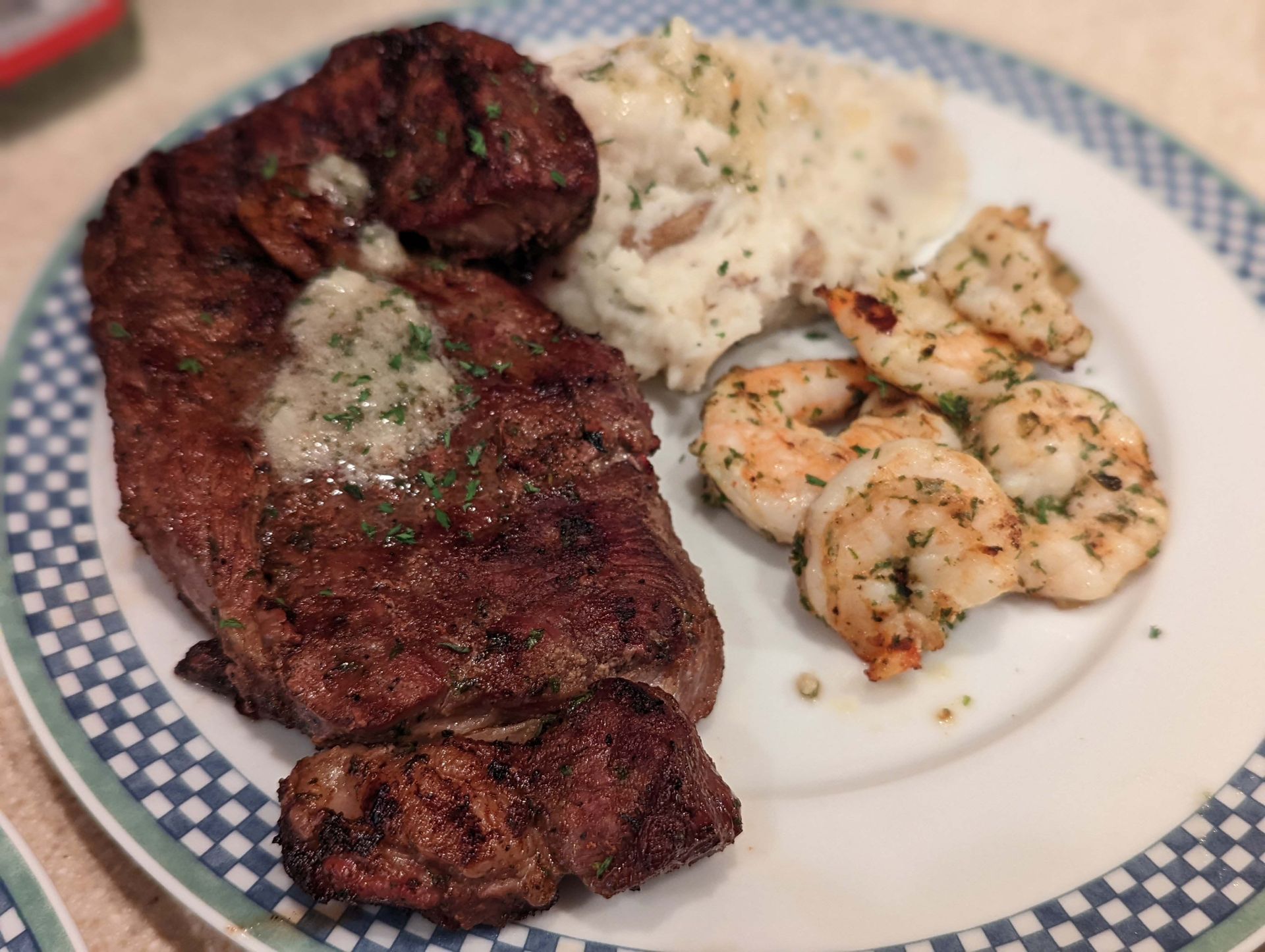 A white plate topped with a steak shrimp and mashed potatoes