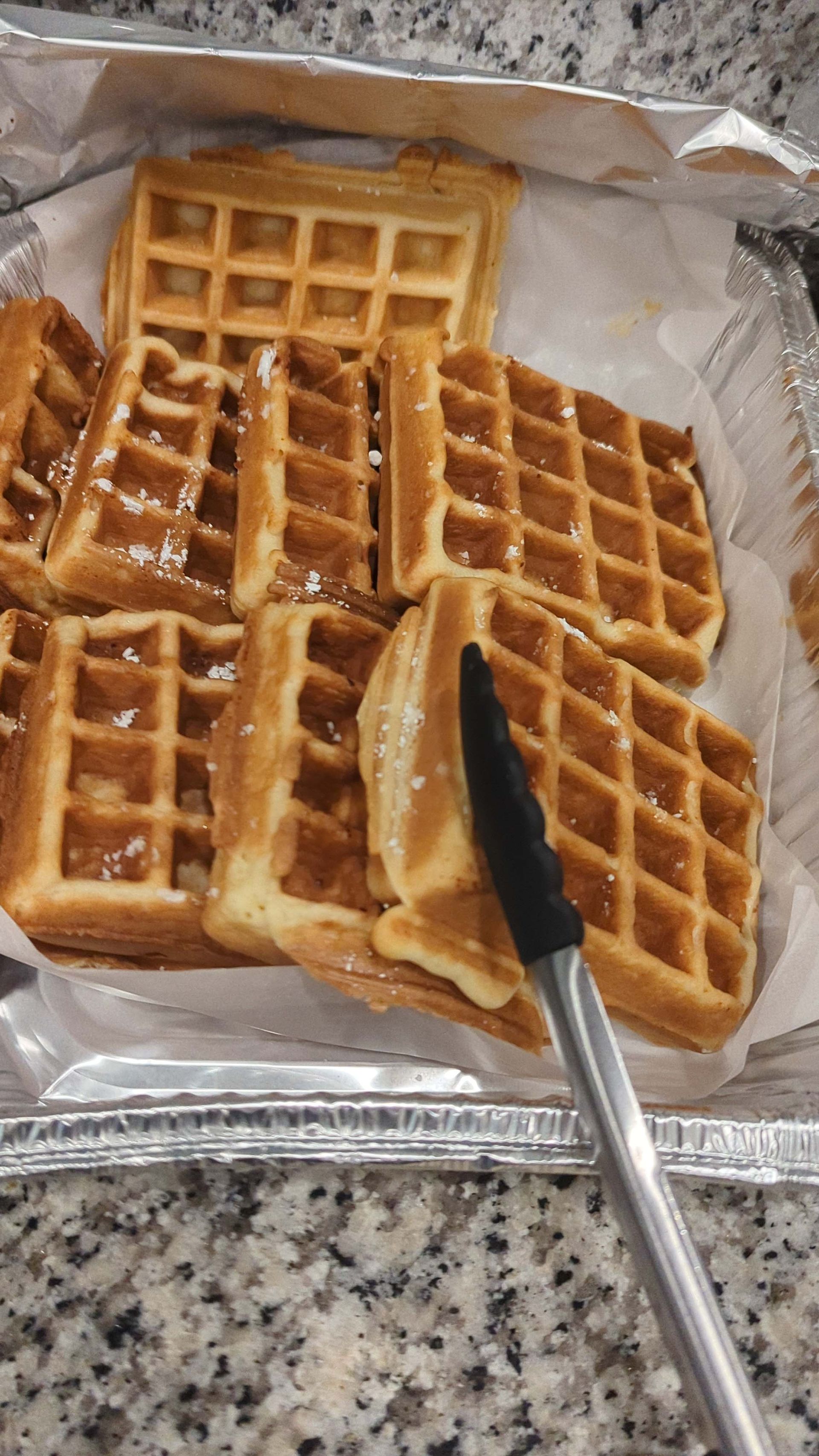 A tray of waffles with tongs on a counter.