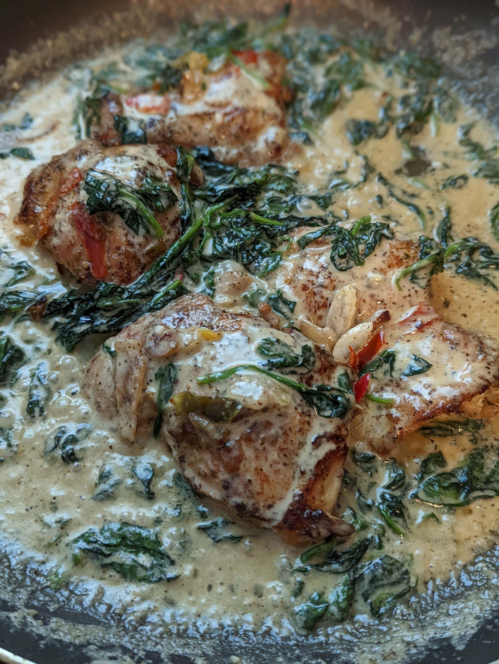 A close up of a pan filled with chicken and spinach in a creamy sauce.